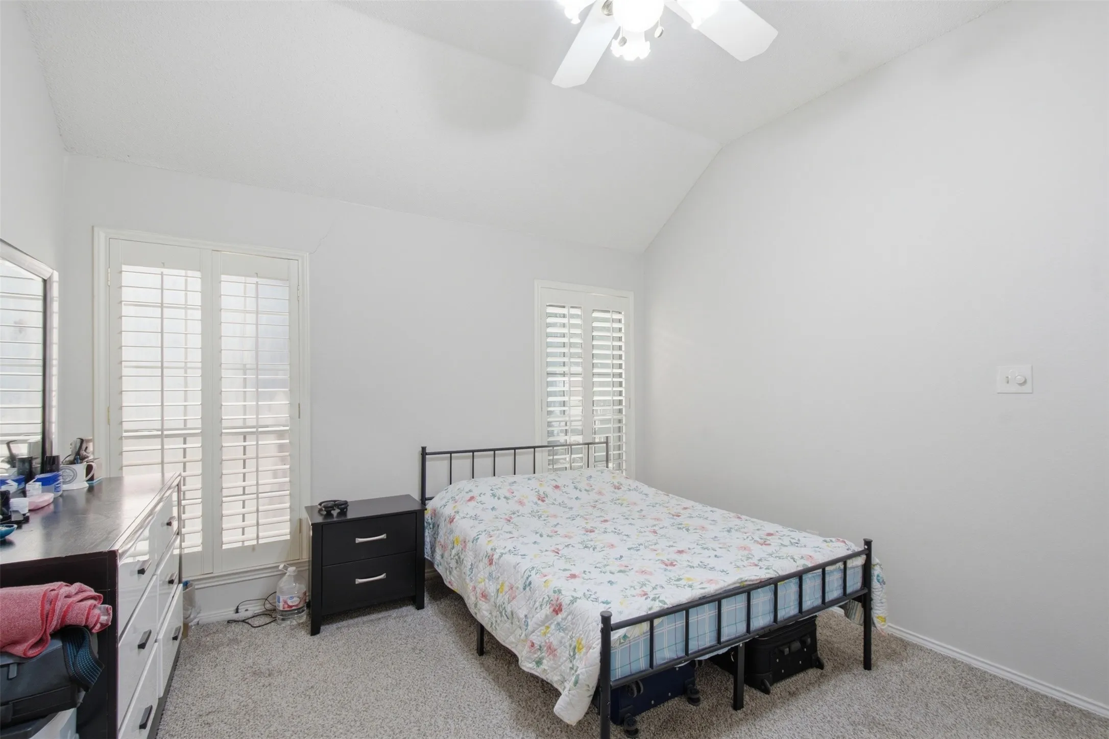 Vaulted ceiling, ceiling fan, carpet flooring, plantation shutters, and light gray wall paint