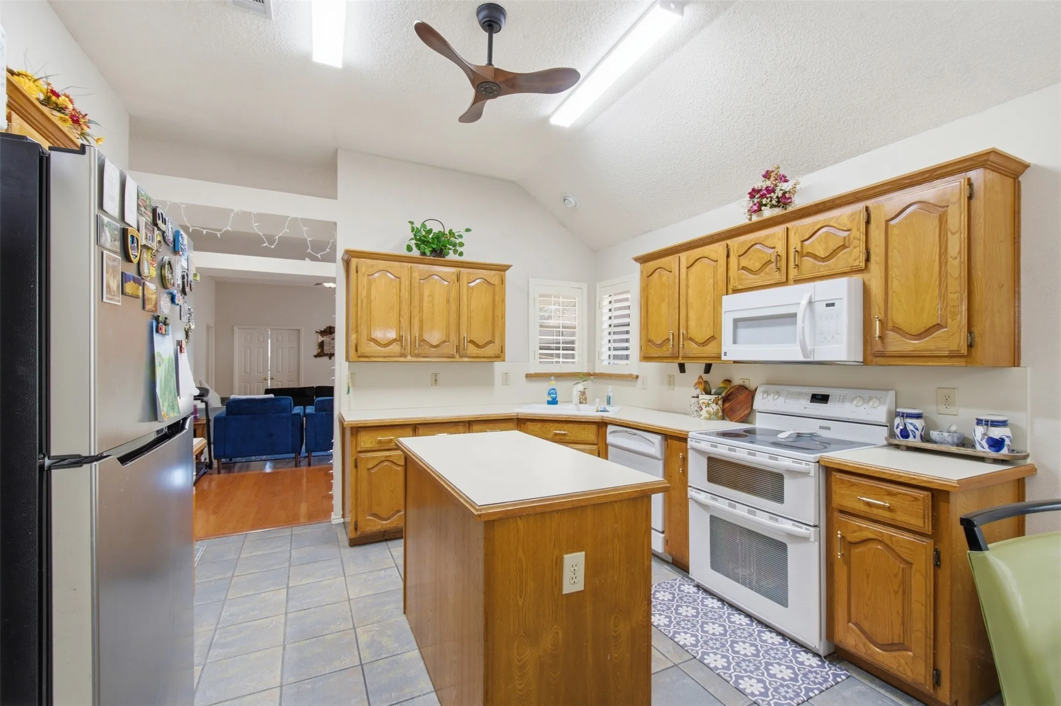Kitchen featuring vaulted ceilings, wood cabinetry, tile flooring, a center island, and white appliances