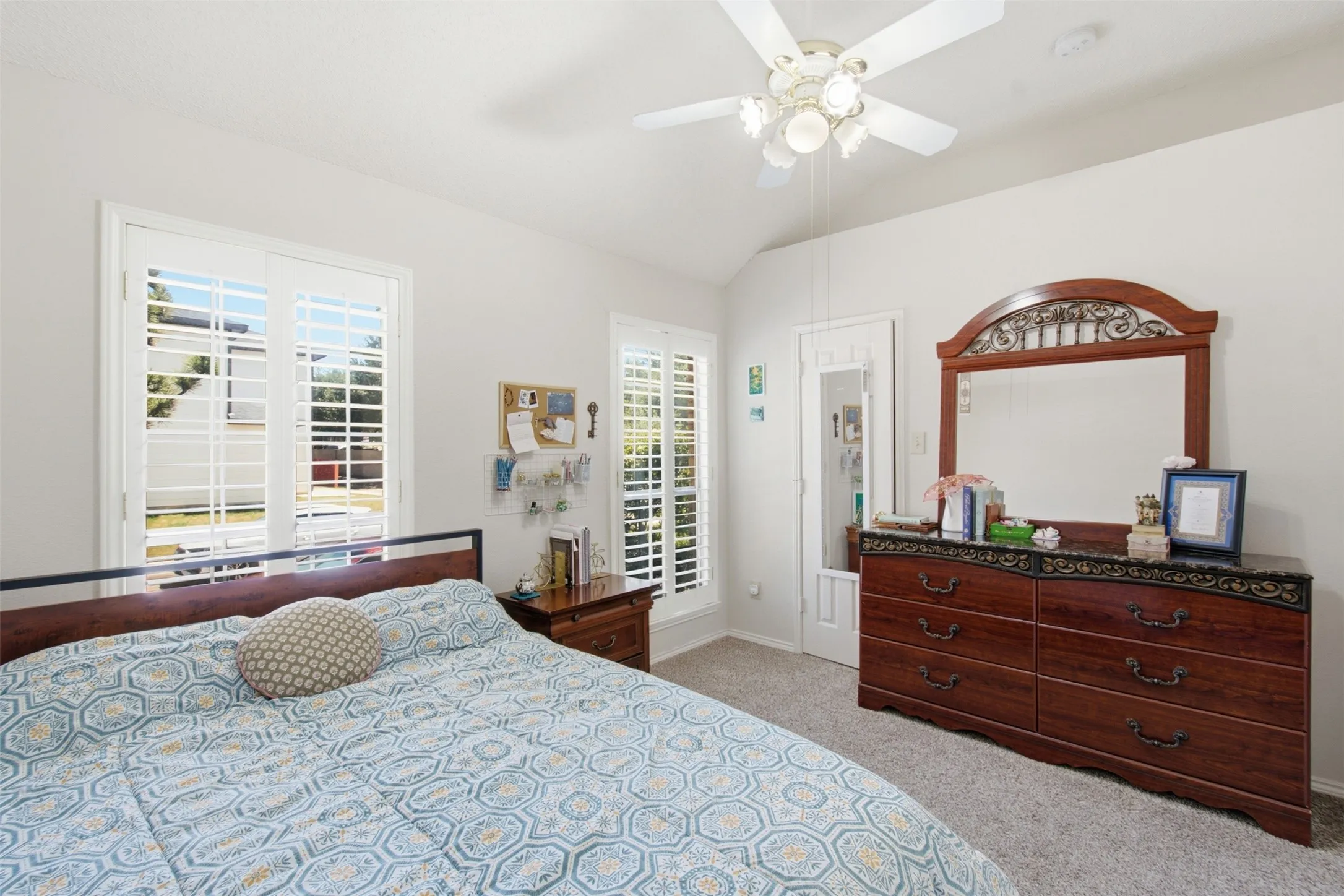 Vaulted ceiling, ceiling fan with integrated lighting, plantation shutters, and carpet flooring
