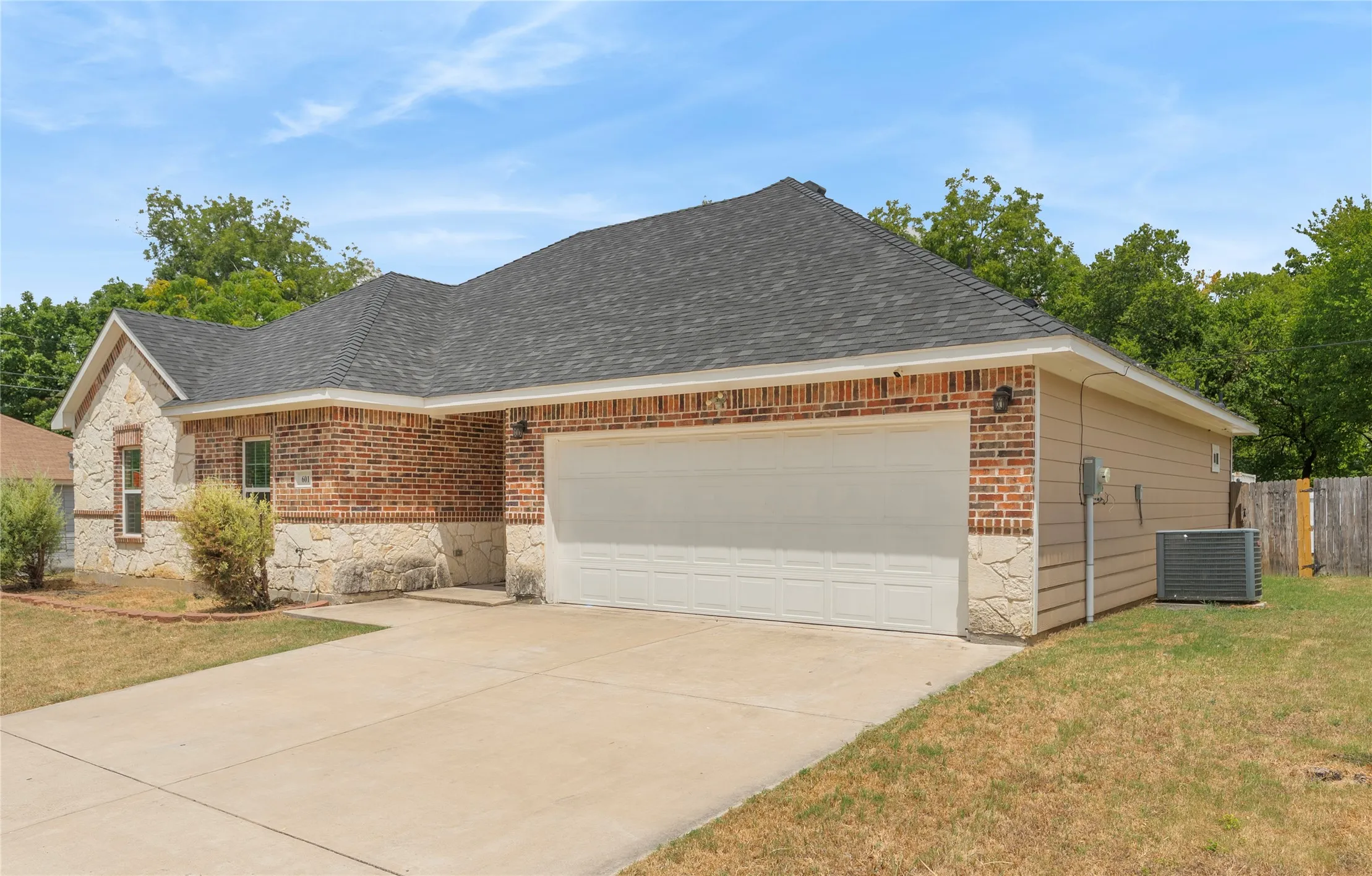 Brick and stone exterior with a two-car garage, concrete driveway, and a shingle roof