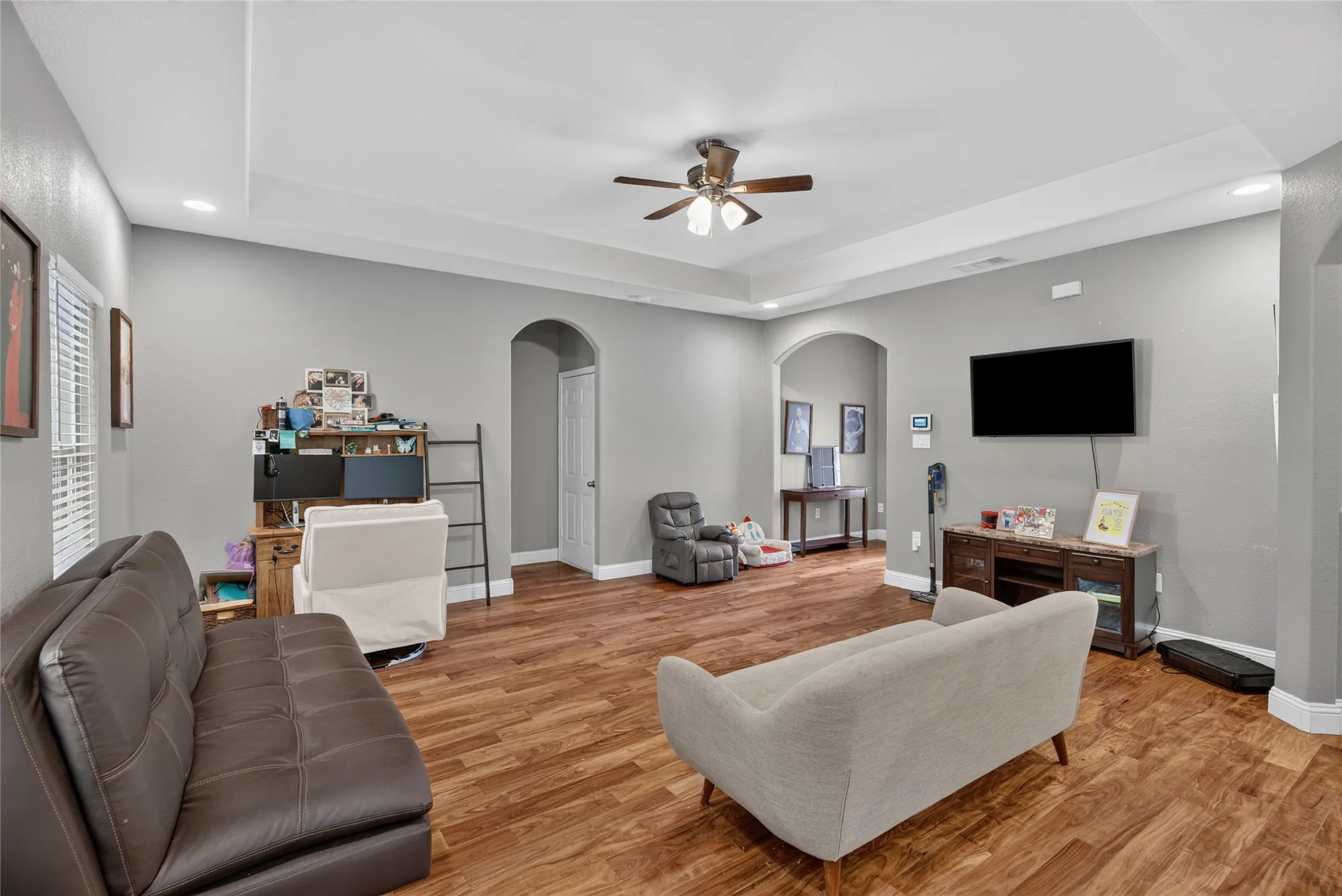 Spacious living area featuring wood-finish flooring, tray ceiling, recessed lighting, and arched doorways
