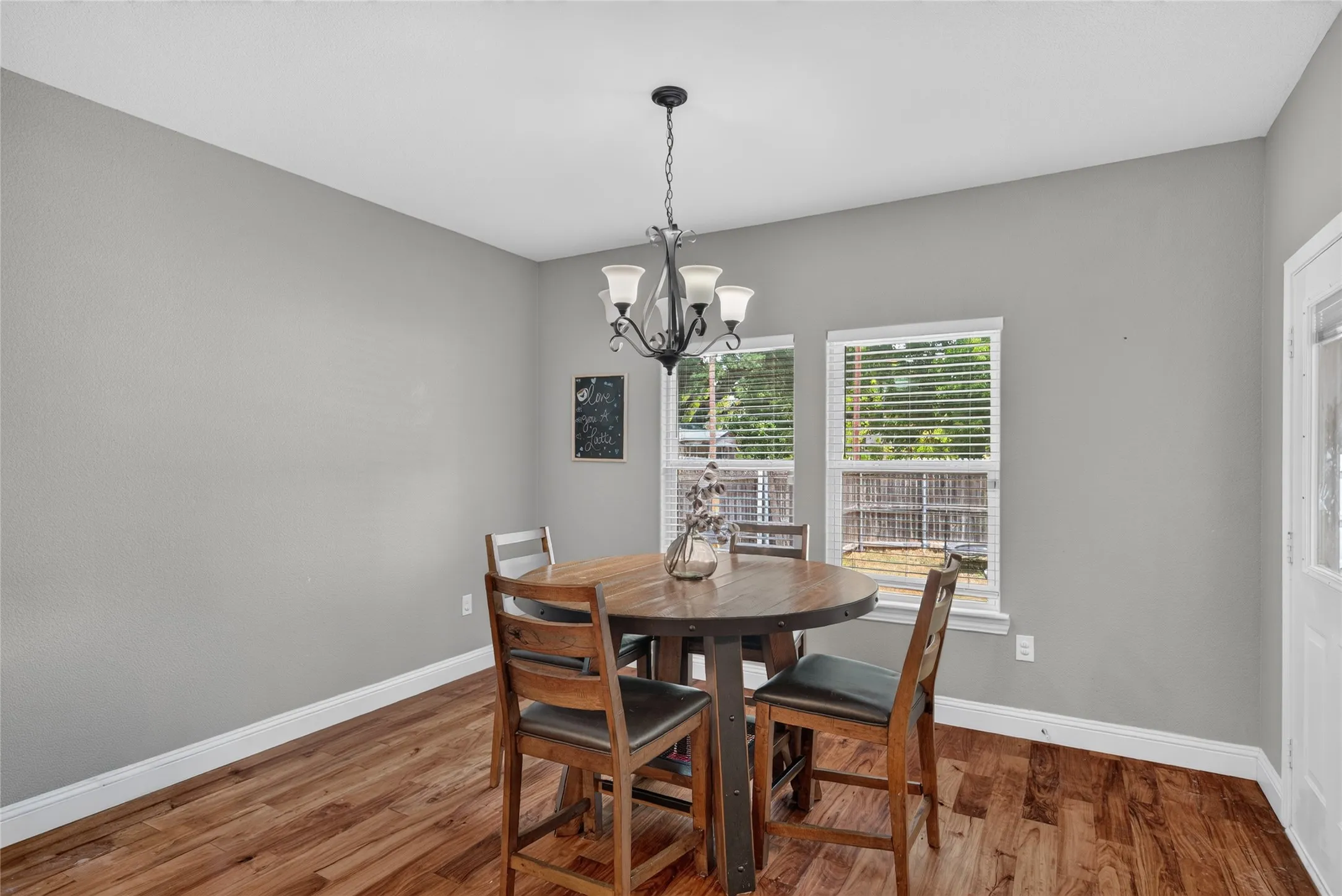 Wood-finish flooring, overhead chandelier, and multiple windows with horizontal blinds