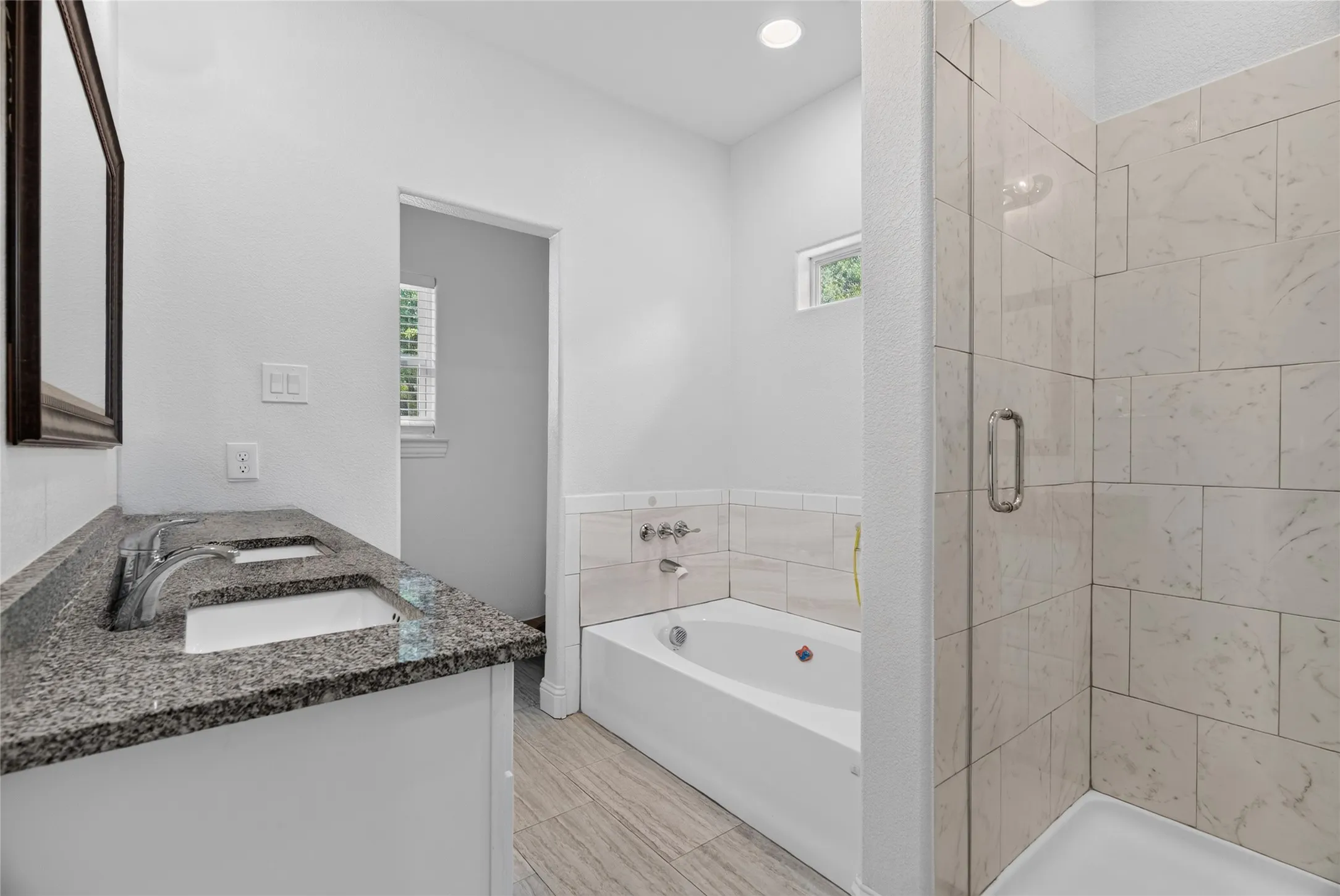 Dual vanity with stone countertop, built-in bathtub, and walk-in shower with tile surround