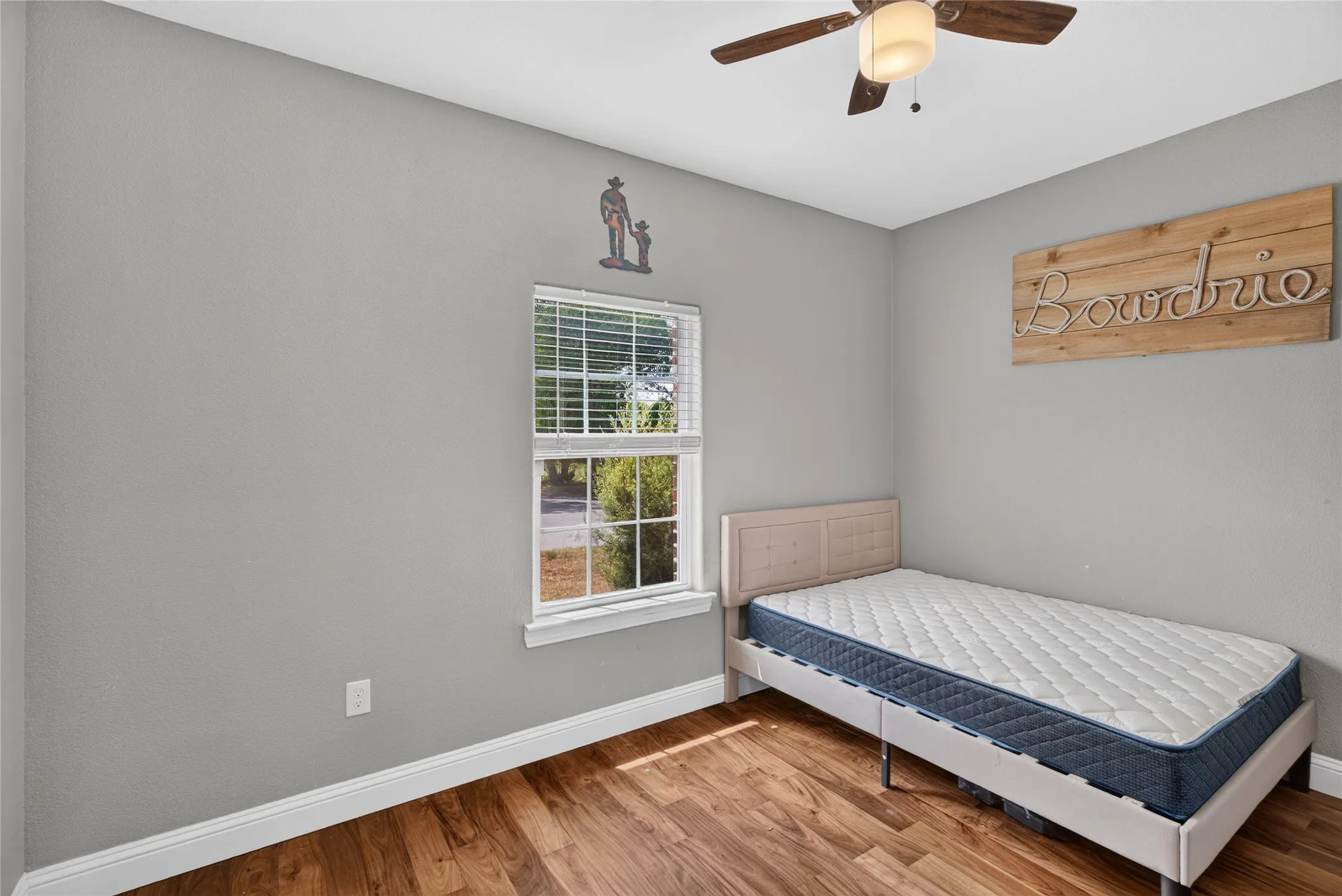Wood-finish flooring, single window with blinds, ceiling fan with integrated lighting, and light grey wall finishes