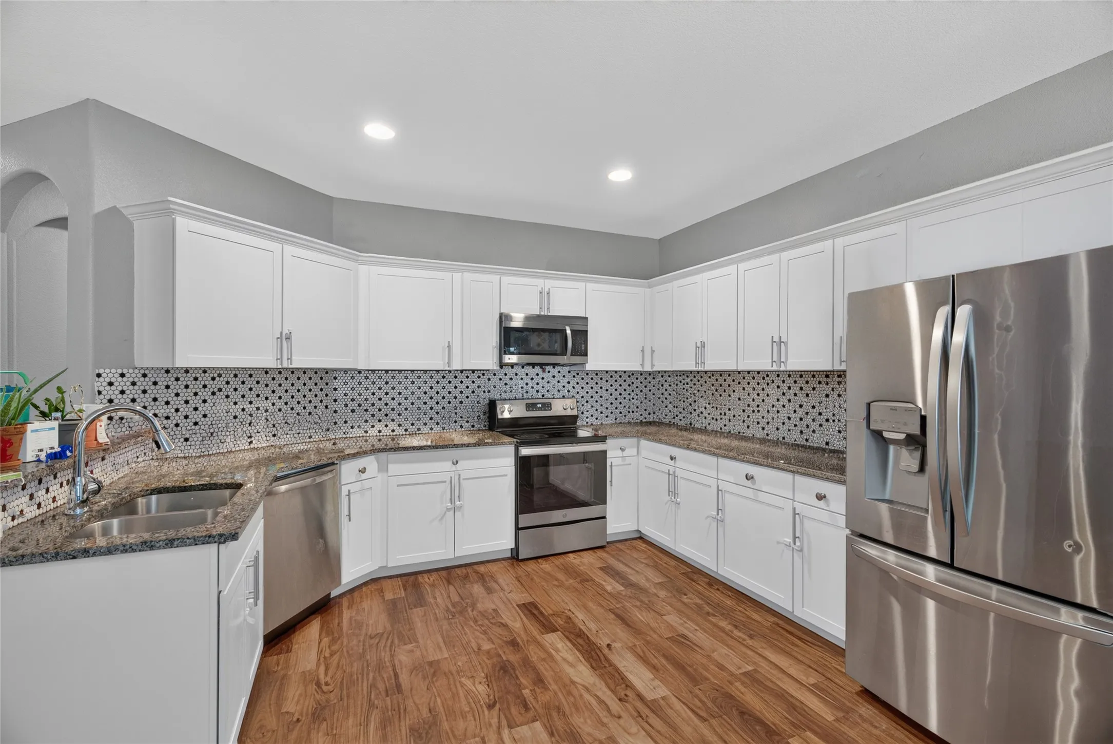 Kitchen featuring white cabinetry, wood-finish flooring, stainless steel appliances, granite countertops, and a patterned tile backsplash