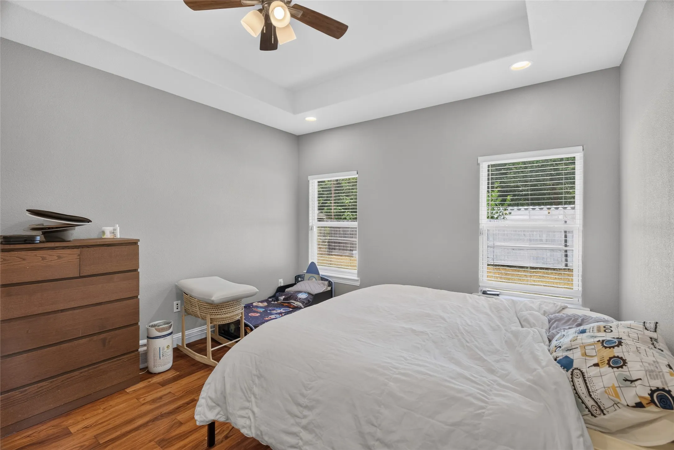 Tray ceiling with recessed lighting, wood-finish flooring, and a ceiling fan
