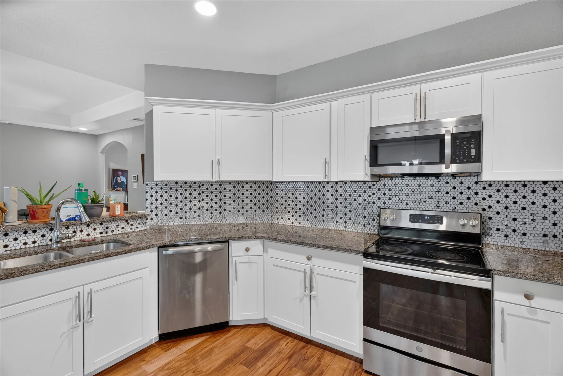 White shaker-style cabinetry, stainless steel appliances, dark stone-finish countertops, mosaic tile backsplash, and wood-finish flooring