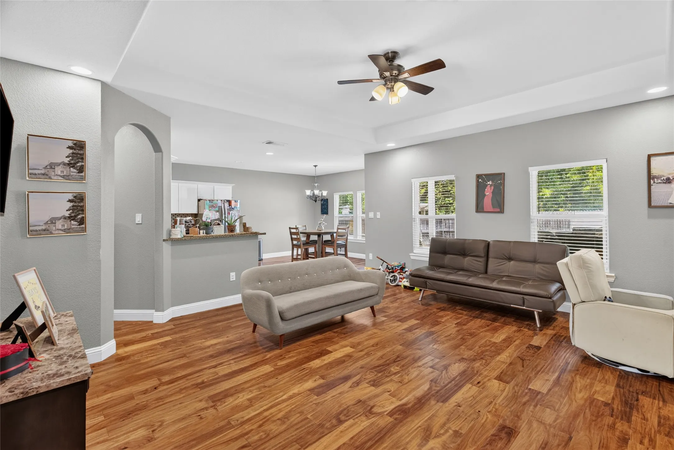 Tray ceiling with recessed lighting and a ceiling fan, wood-finish flooring, and an arched doorway
