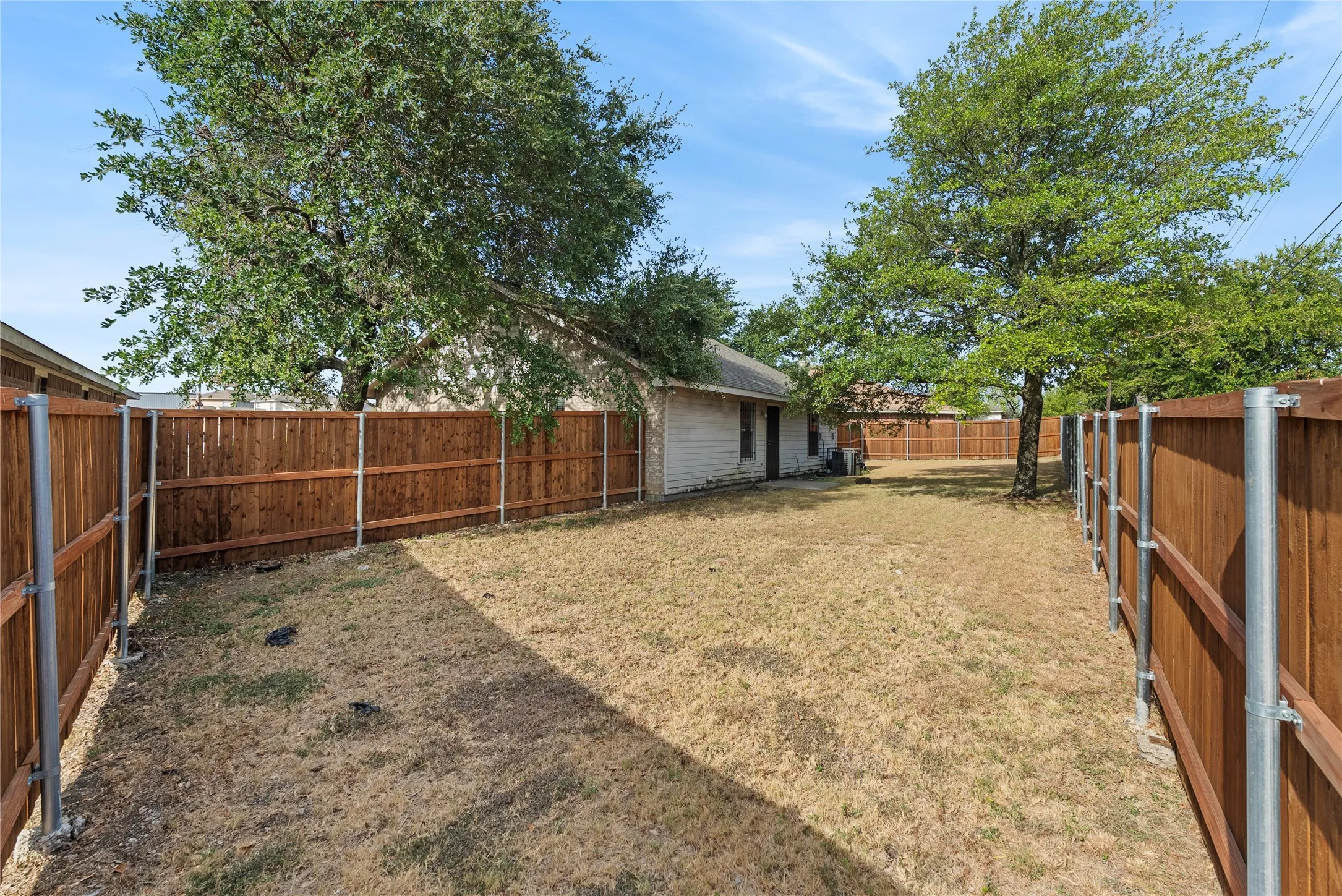 Fenced backyard featuring mature trees and a single-story structure