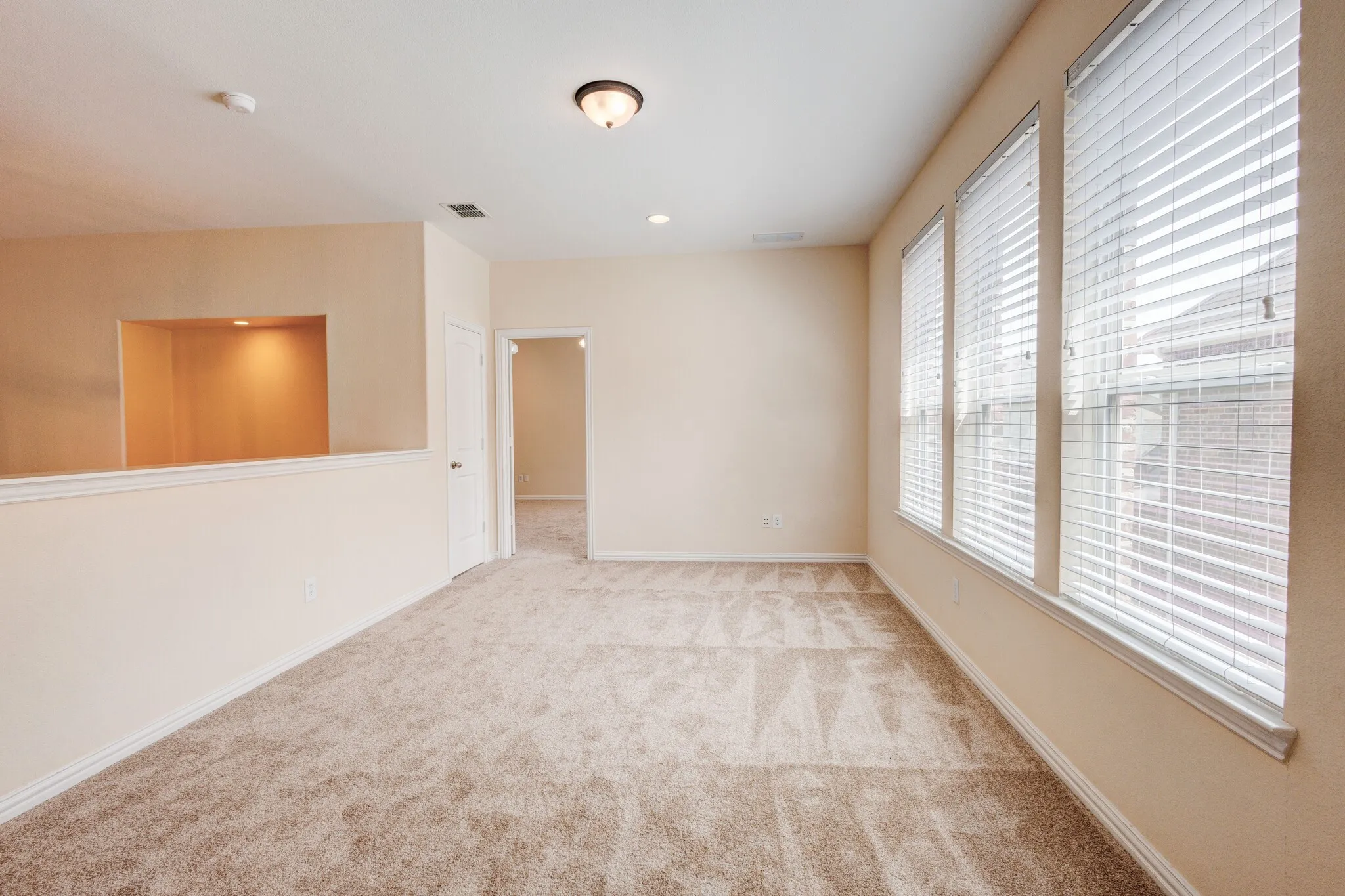 Carpeted room featuring a recessed architectural niche with accent lighting, three large windows, and a flush mount ceiling light