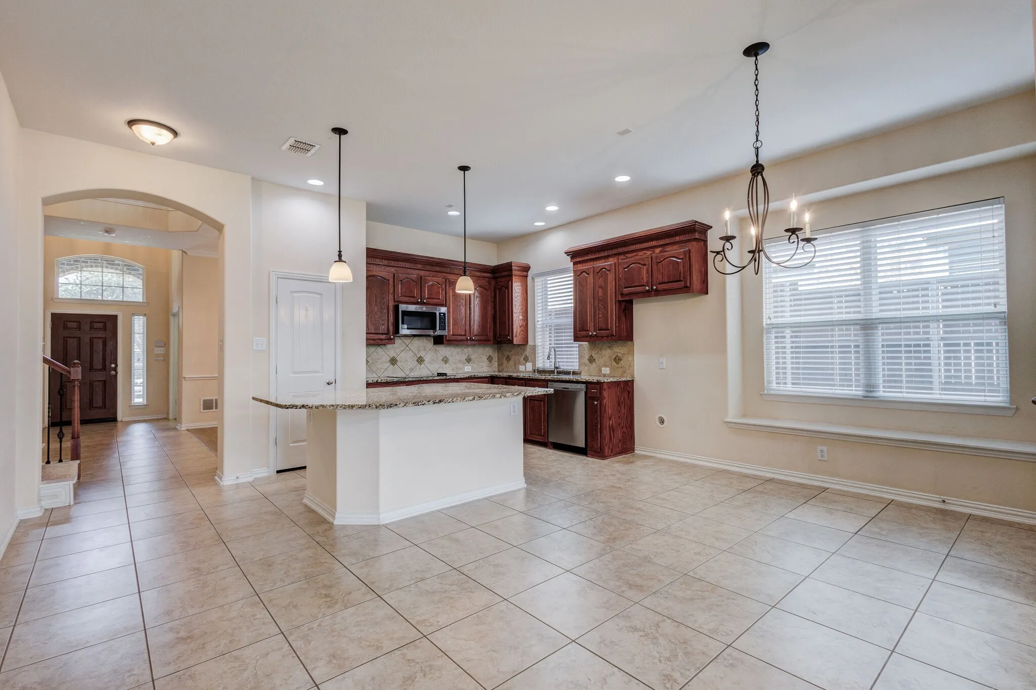 Open-concept layout featuring tile flooring, a kitchen island with pendant lighting, dark wood-finish cabinetry, and stainless steel appliances