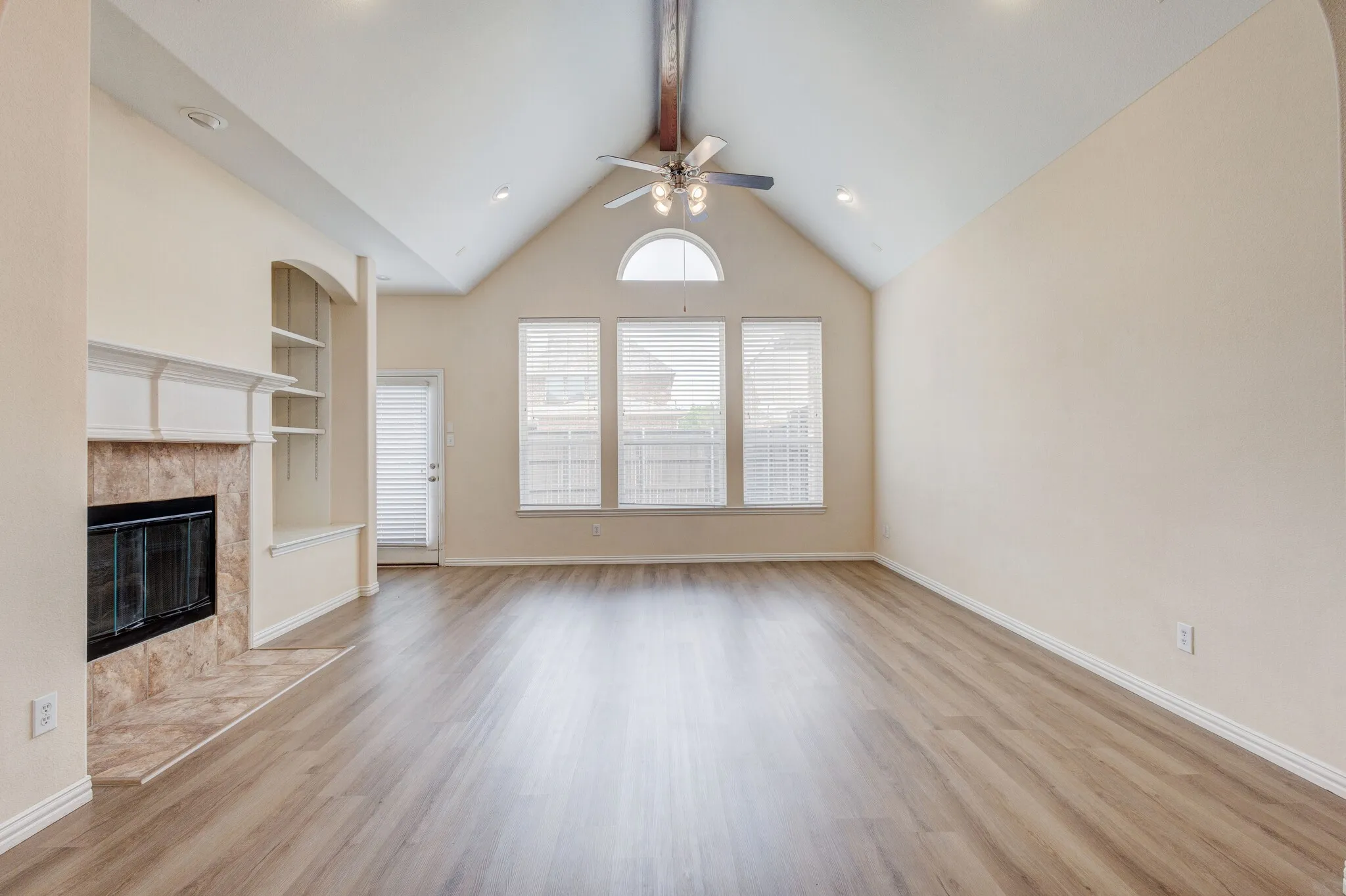 Vaulted ceiling, wood-finish flooring, fireplace with stone surround, built-in shelving, and ceiling fan
