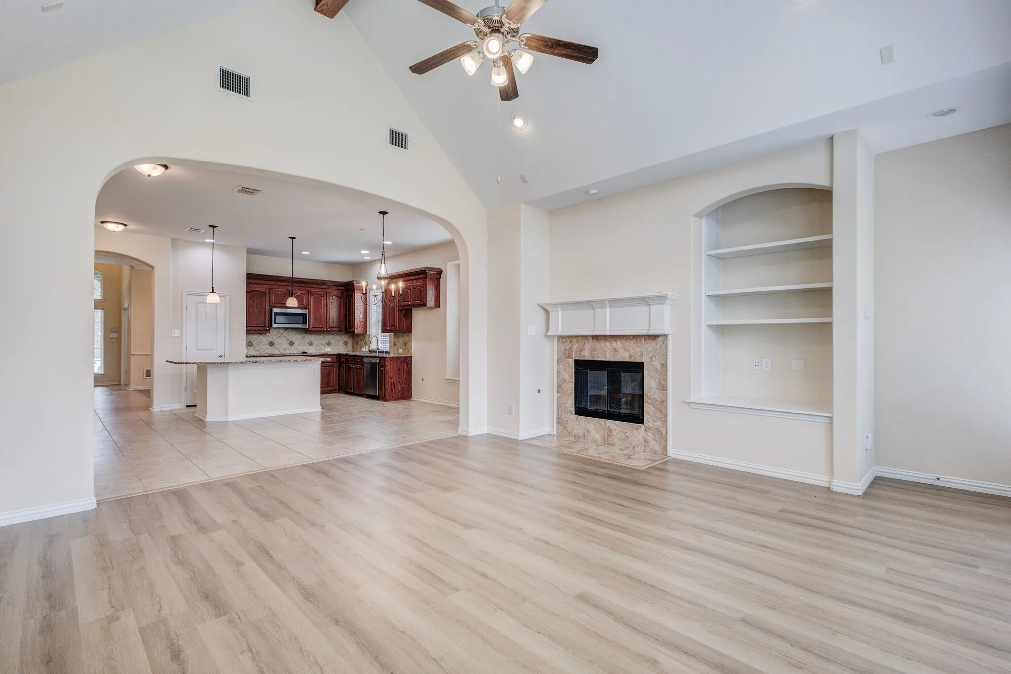 Vaulted ceiling with a ceiling fan, wood-finish flooring, built-in shelving, stone-clad fireplace, and arched entryways