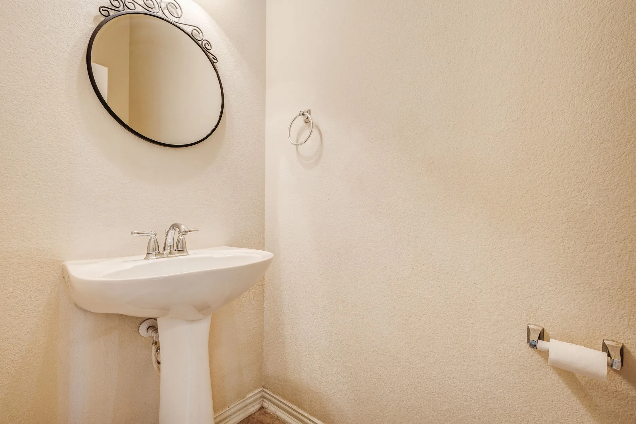 Pedestal sink with chrome faucet, oval wall mirror, and neutral wall finish