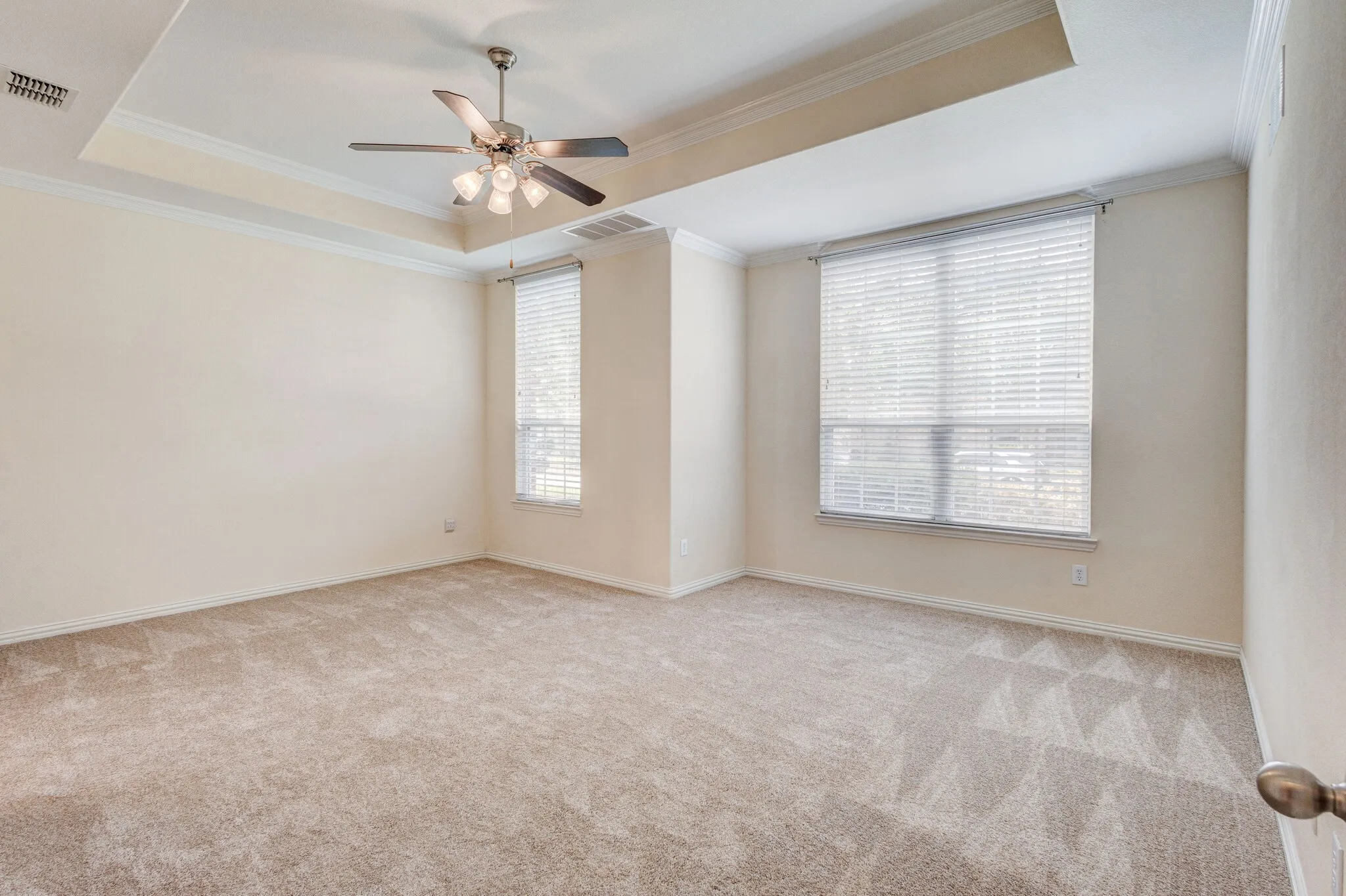 Tray ceiling with crown molding, ceiling fan with integrated lighting, carpeted flooring, and two windows with blinds