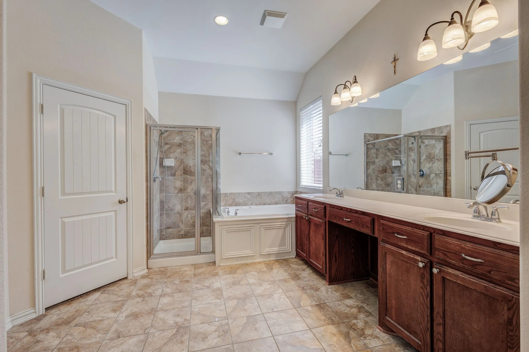Tiled flooring with a glass-enclosed shower, a built-in bathtub, and an extended vanity with dual sinks