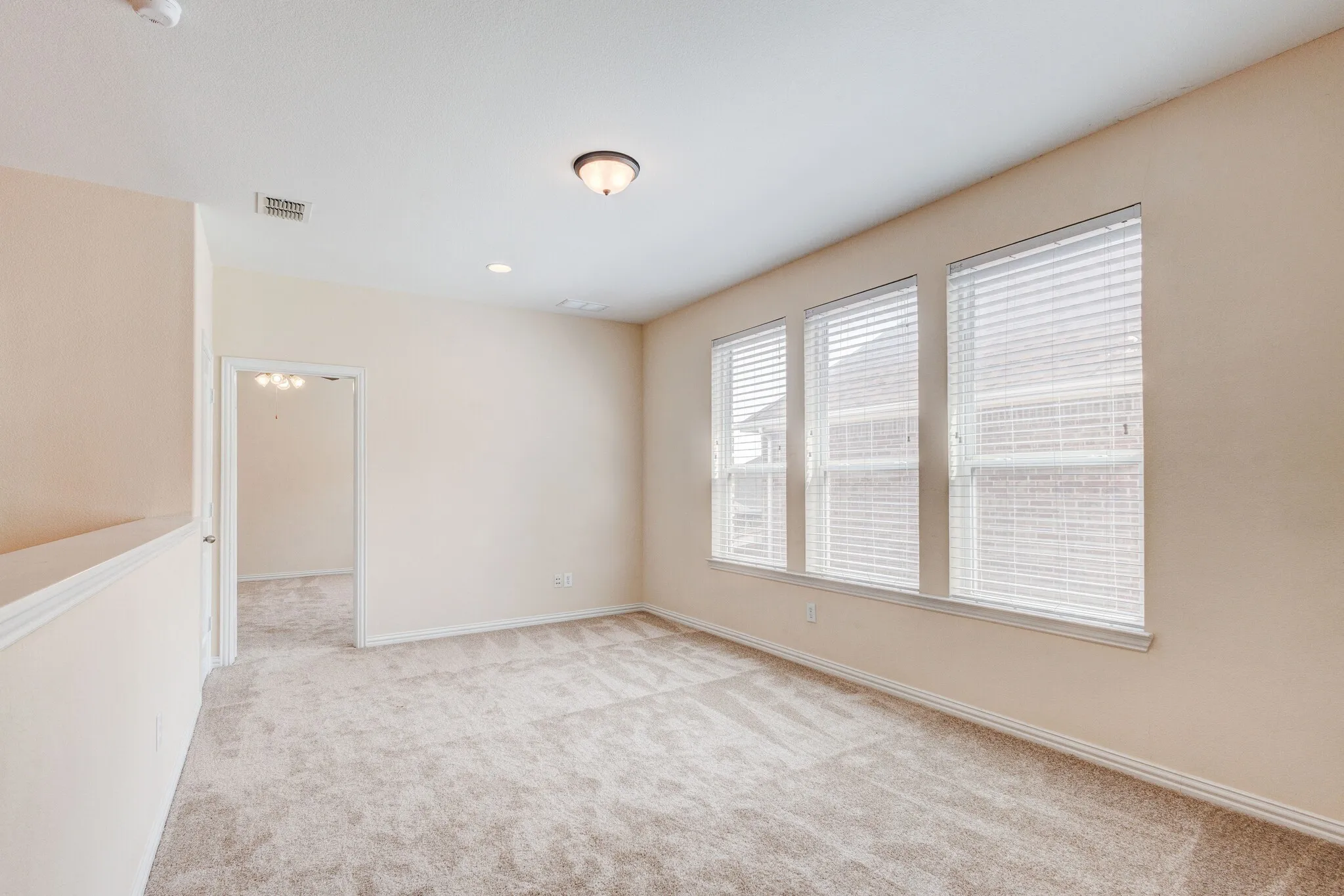Neutral wall paint, plush carpeting, three windows with blinds, ceiling-mounted light fixture, and recessed lighting