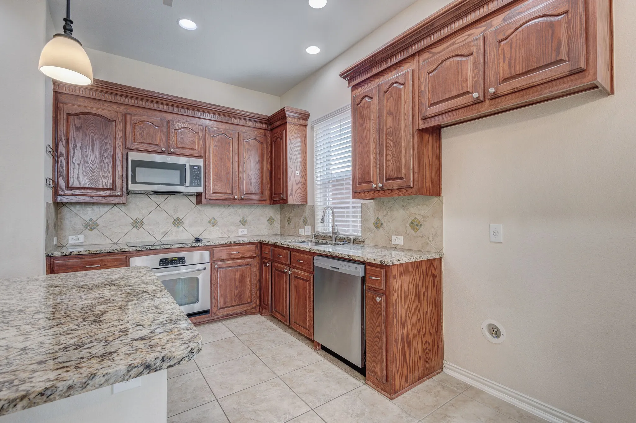 Kitchen featuring wood cabinetry, stainless steel appliances, granite countertops, and a tiled backsplash