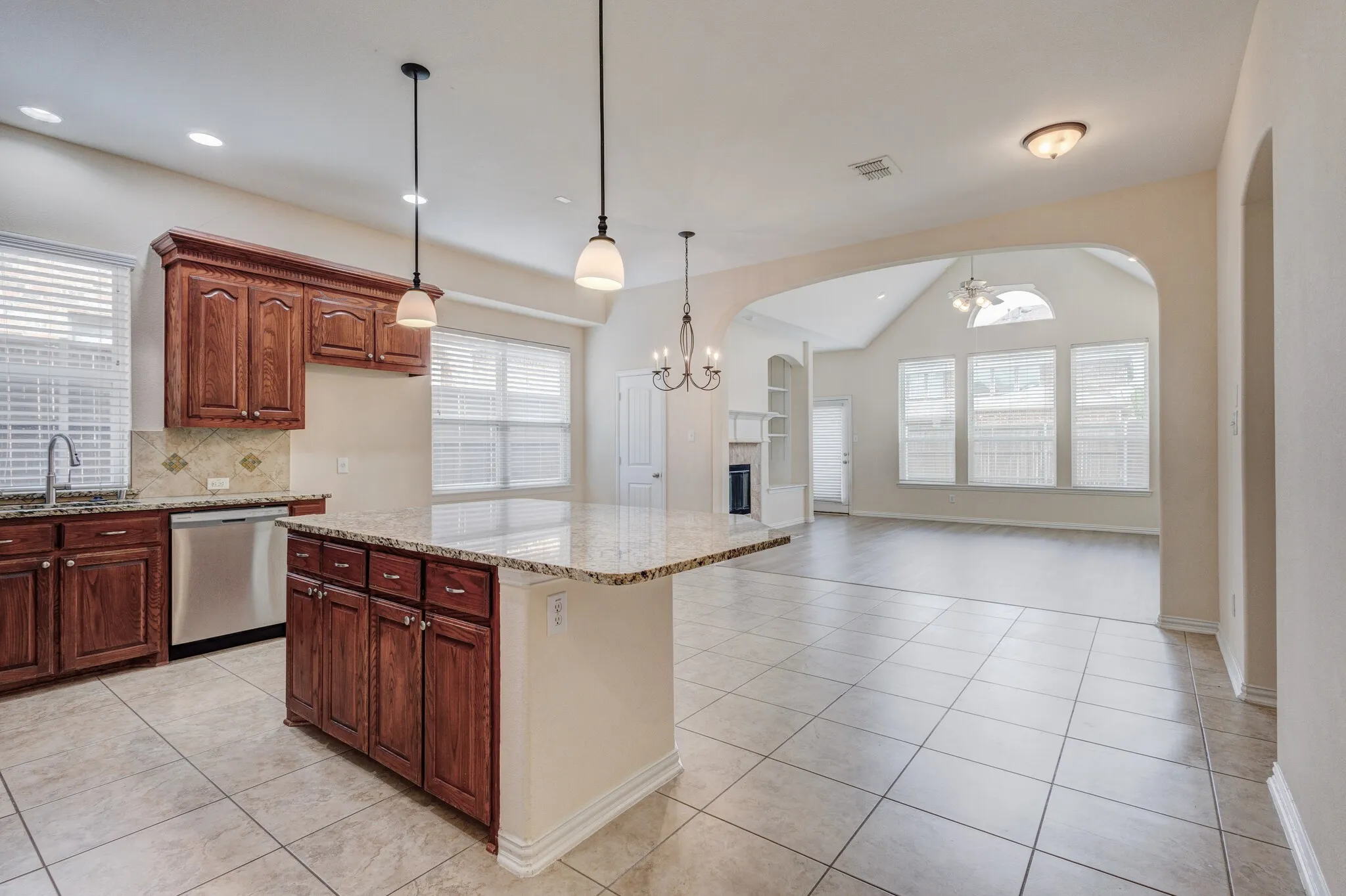 Kitchen island with granite countertop, recessed lighting, stainless steel dishwasher, wood-finish cabinetry, and tiled flooring