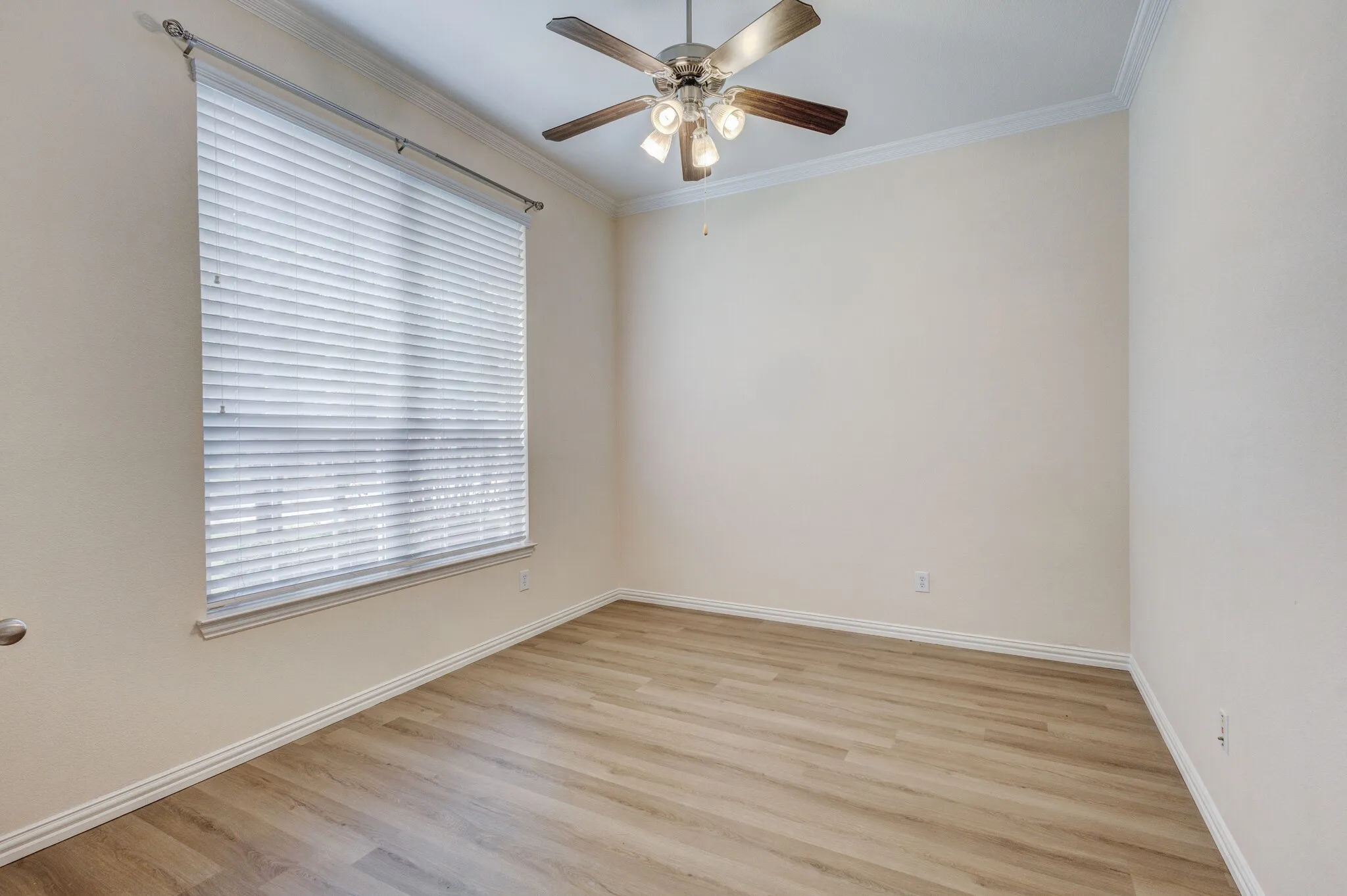 Spacious room featuring a ceiling fan with light kit, wood-finish flooring, crown molding, and a window with blinds