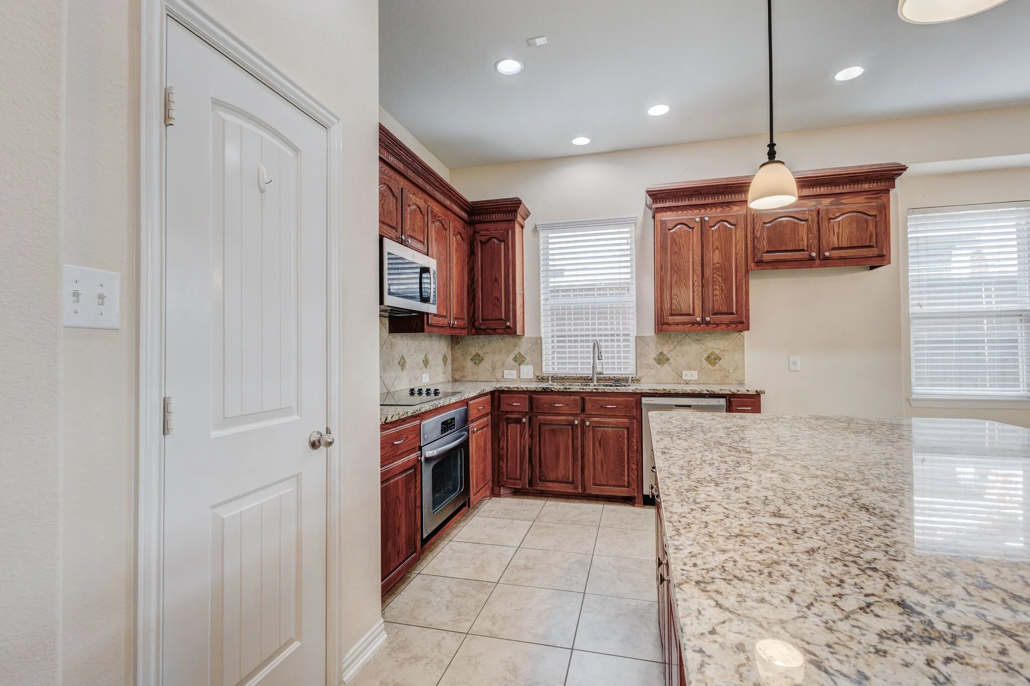 Kitchen featuring wood cabinetry, stainless steel appliances, a tile backsplash, and a large island with a stone countertop