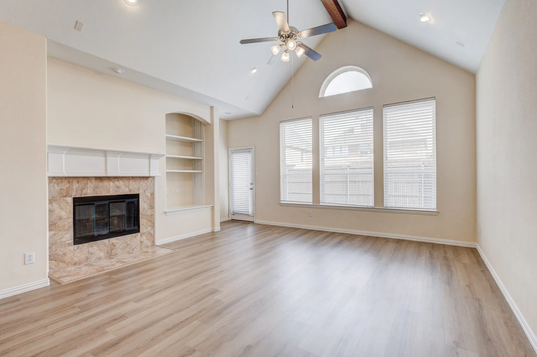 Vaulted ceiling with exposed beam, wood-finish flooring, built-in shelving, fireplace with stone surround, and ceiling fan