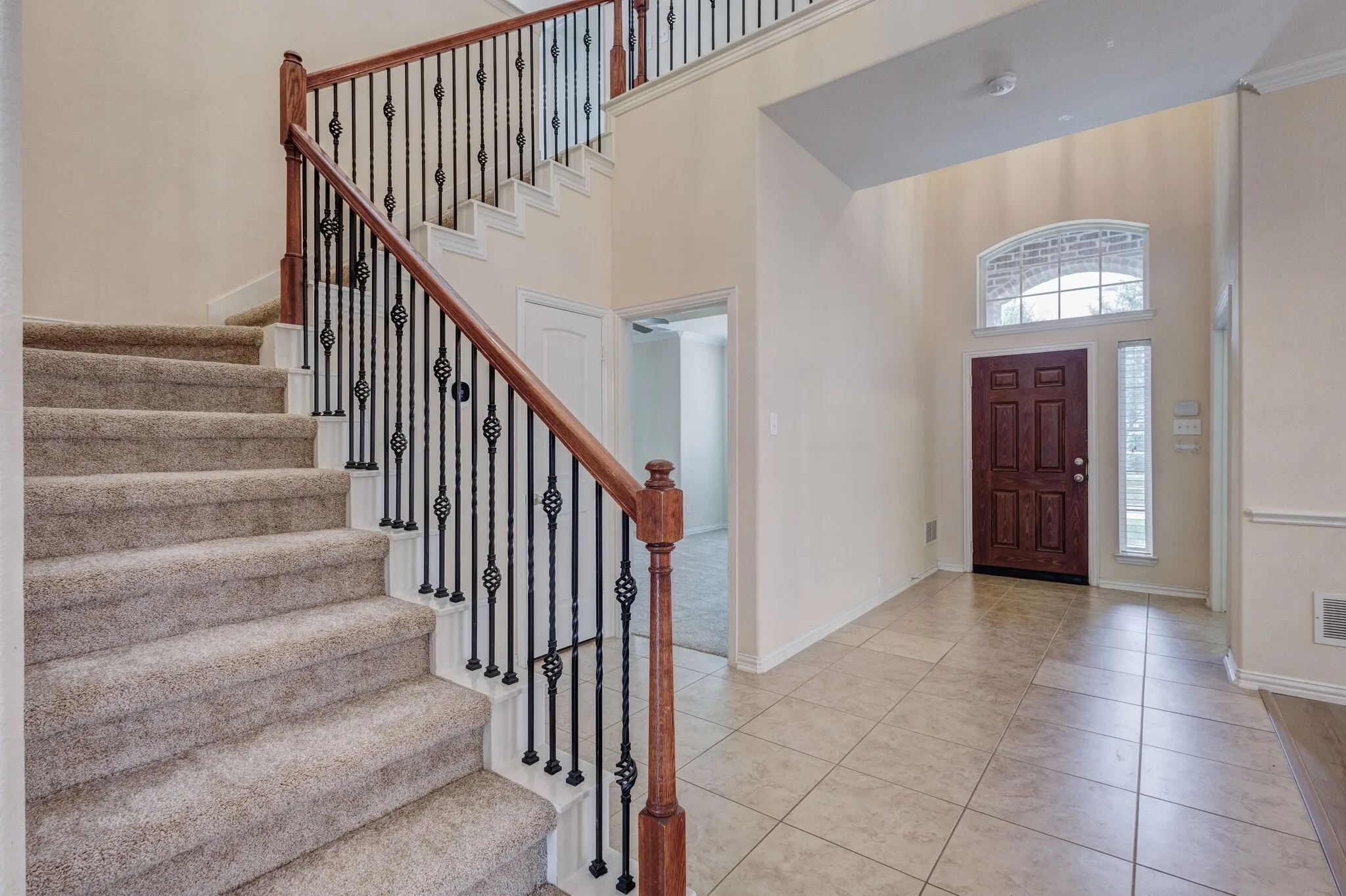 Two-story entryway featuring a wood-panel door, arched transom window, and tiled flooring