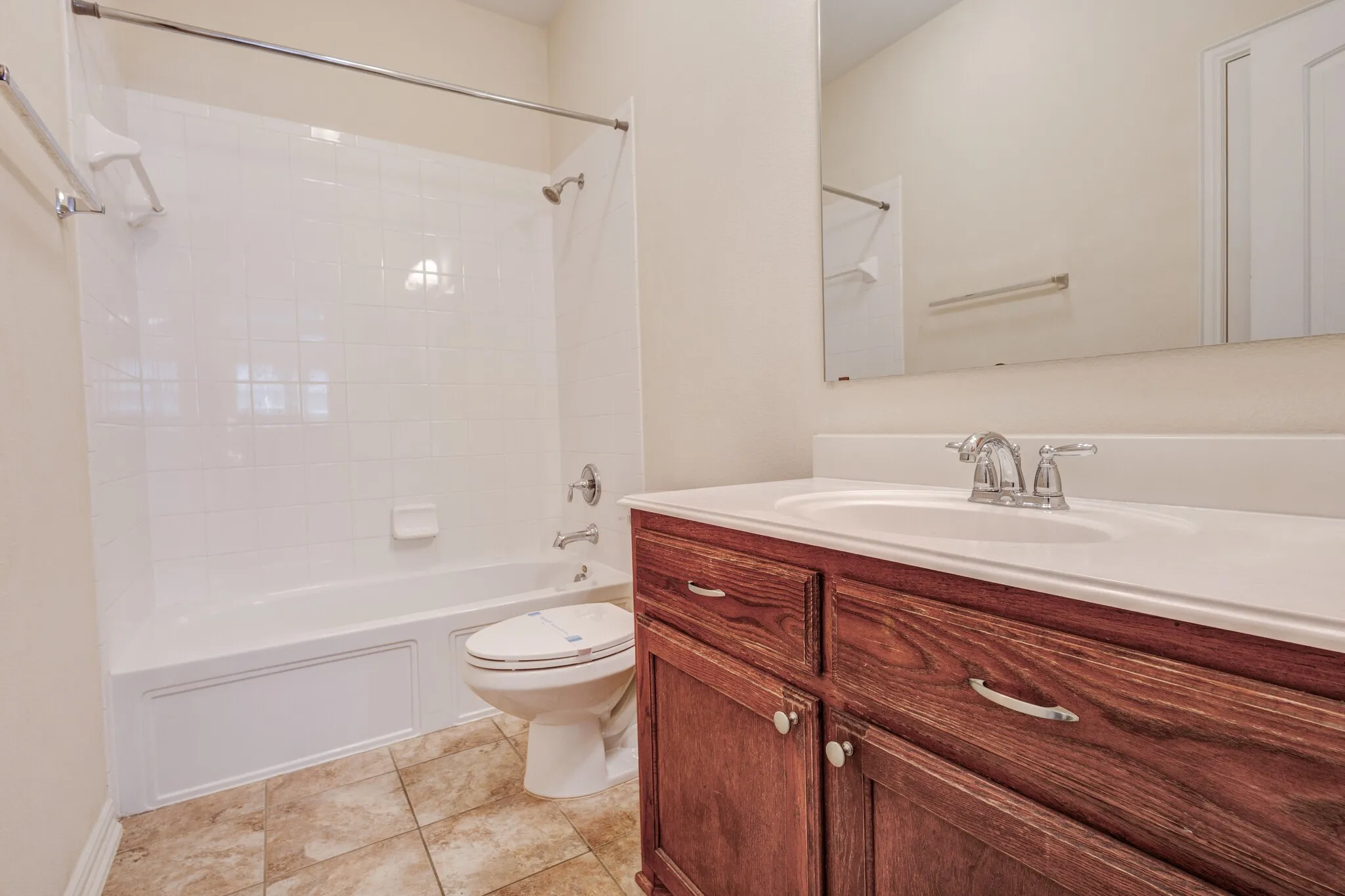 Bathroom featuring a wood-finish vanity with a white countertop, an integrated sink, a full-width mirror, and a shower-tub combination with white tile surround