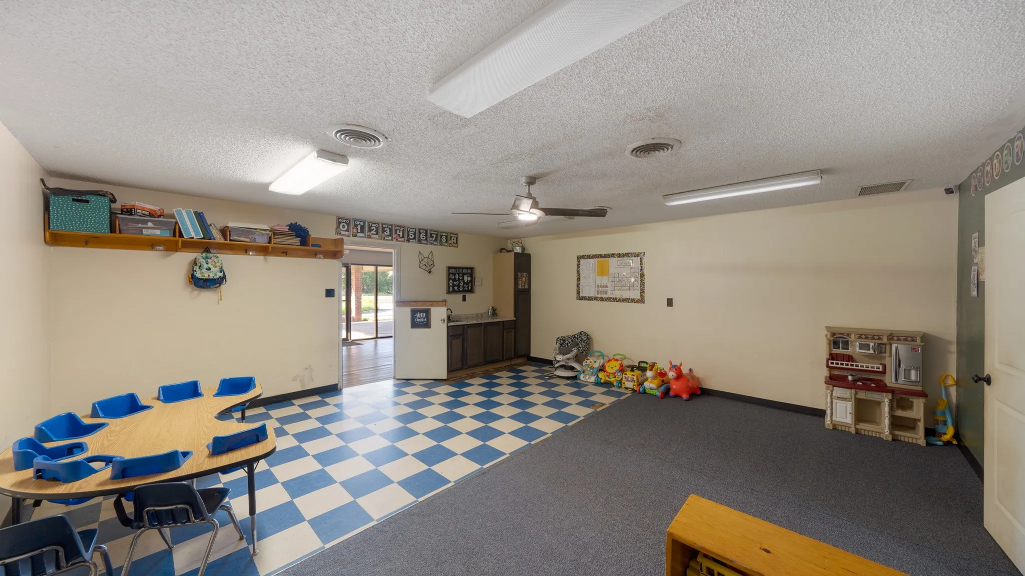 Spacious room featuring mixed flooring, including blue and white checkered pattern and dark gray carpeting