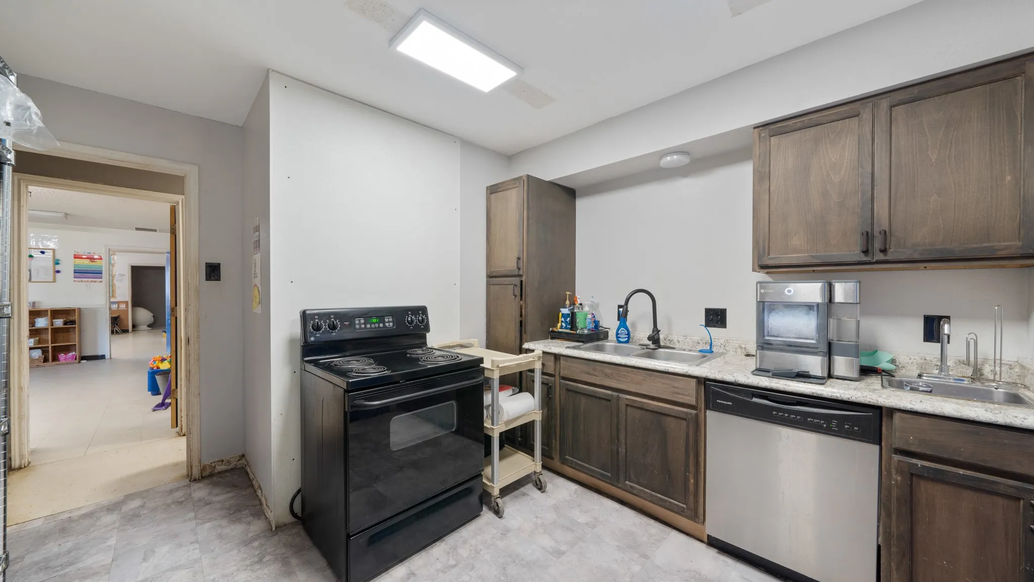 Kitchen featuring wood-finish cabinetry, light-toned countertops, and a stainless steel dishwasher