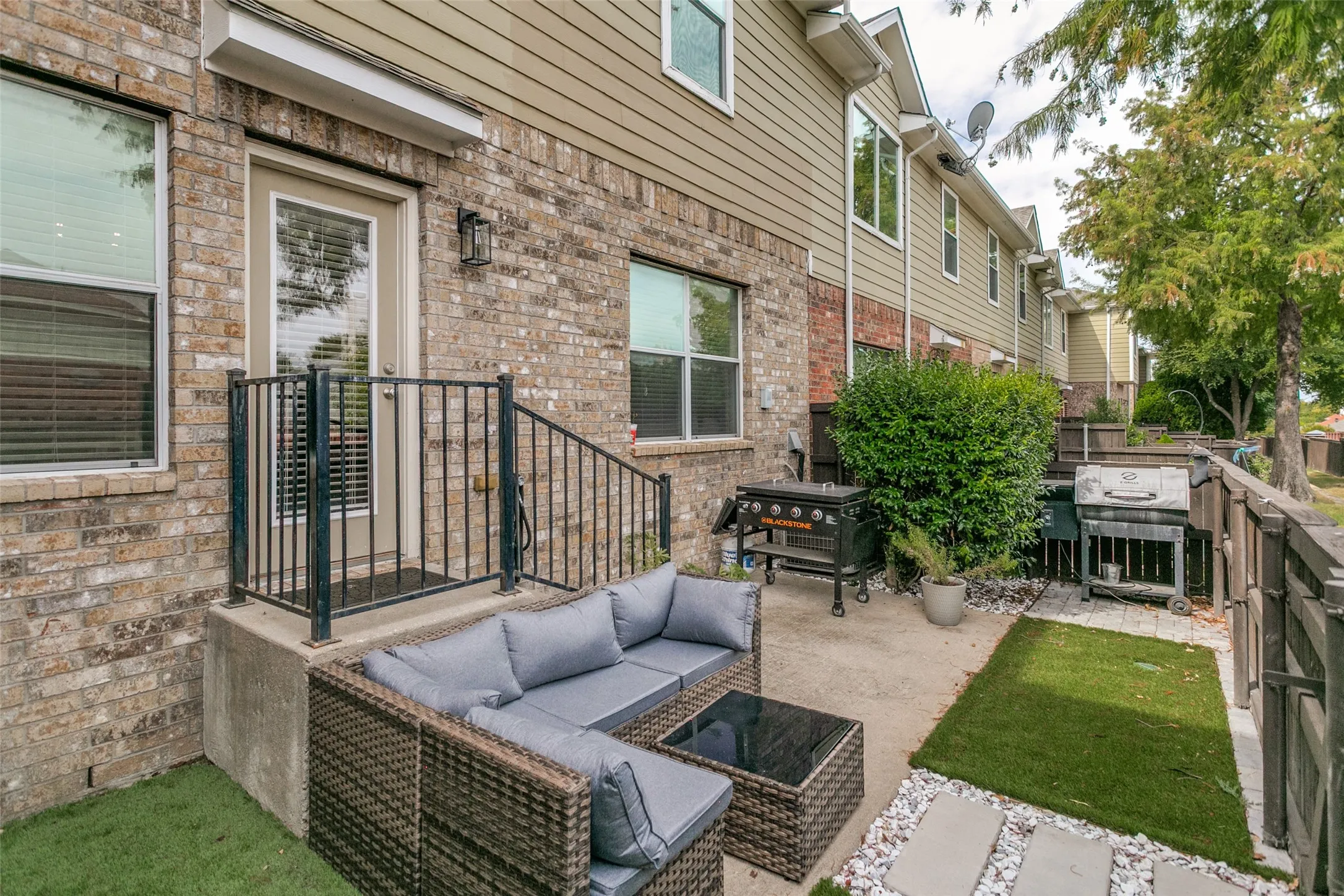 Paved patio with concrete slab and artificial turf elements, featuring a brick and siding exterior