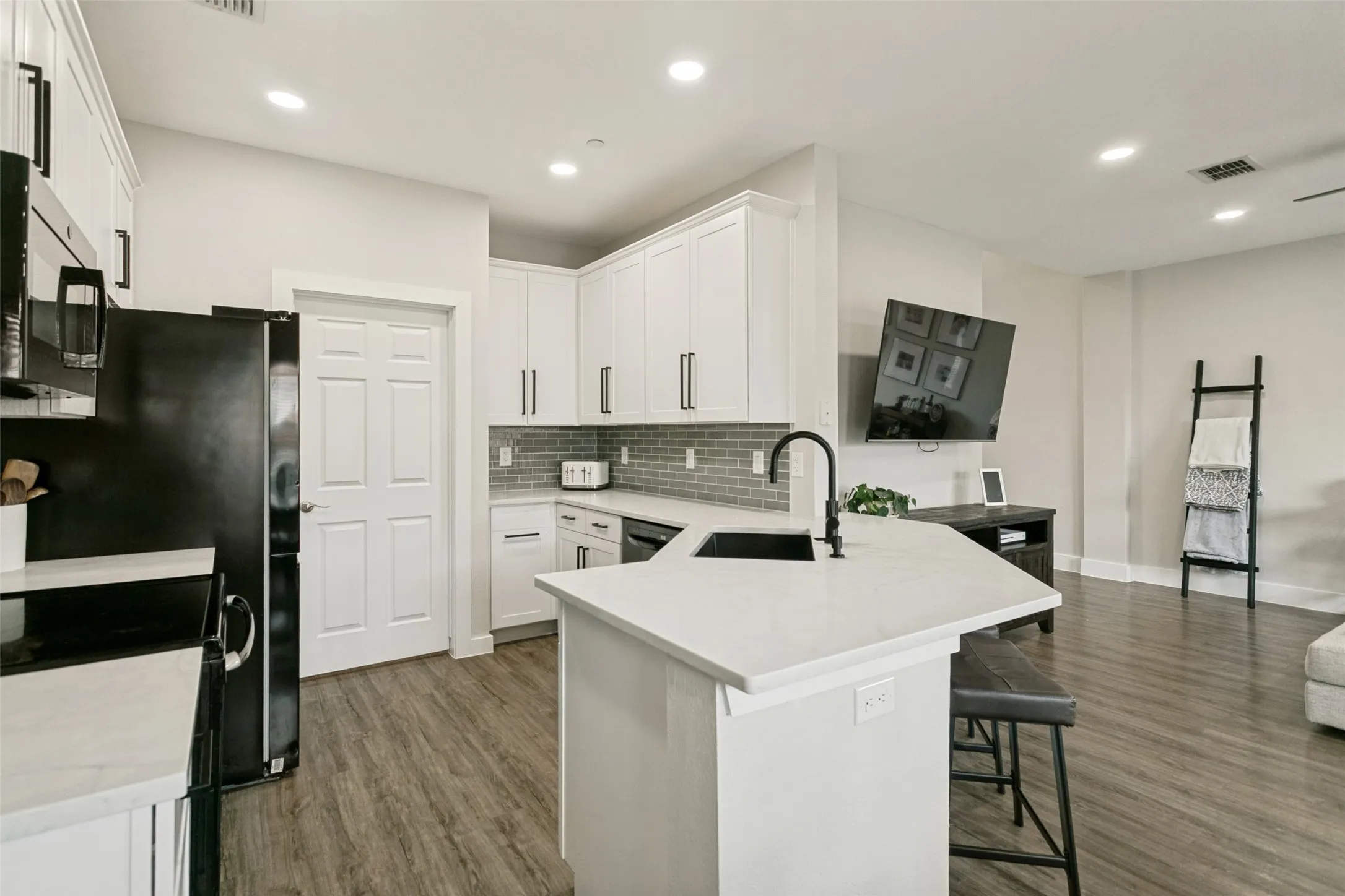 Contemporary kitchen featuring white cabinetry, light countertops, a dark subway tile backsplash, and wood-finish flooring