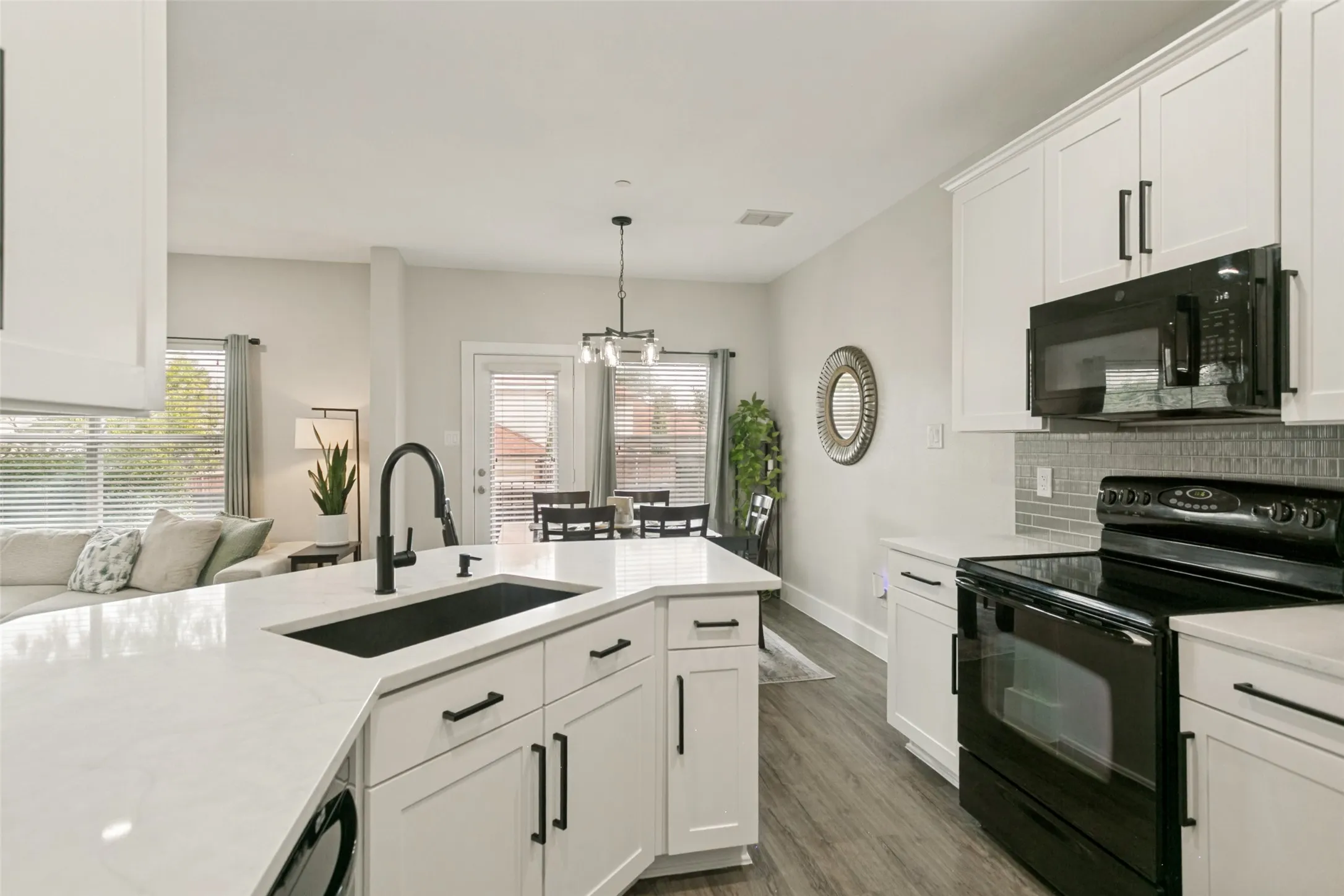 White shaker cabinetry with black hardware, white countertops, black kitchen appliances, and wood-finish flooring