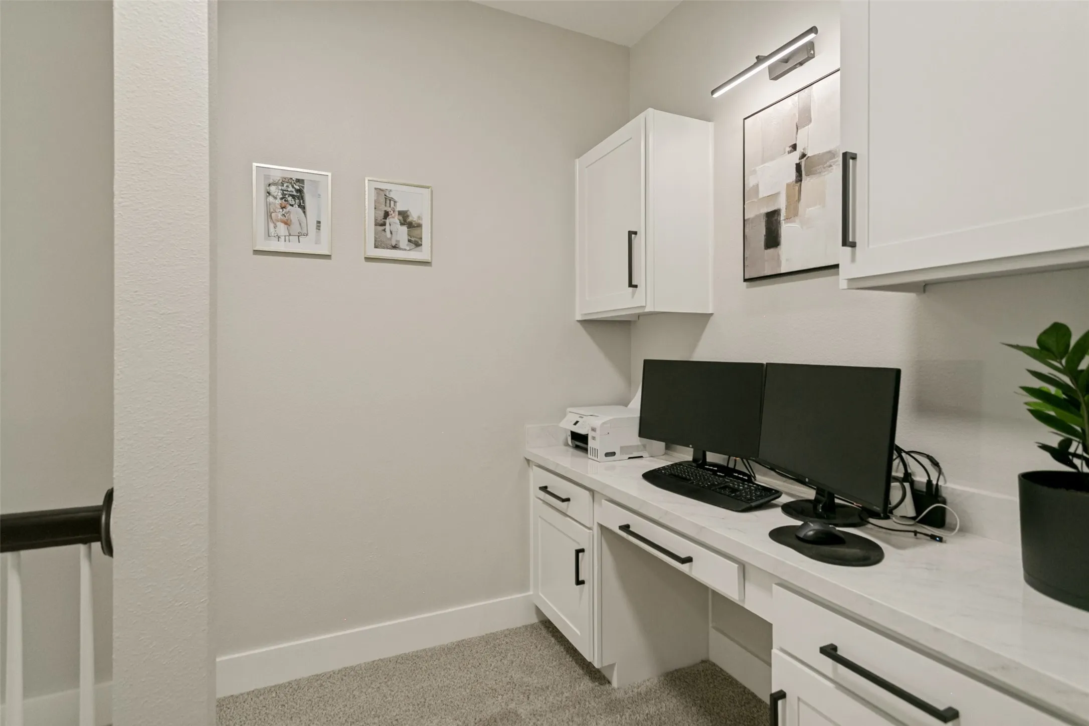 Built-in desk with white cabinetry, black hardware, solid surface countertop, and integrated task lighting