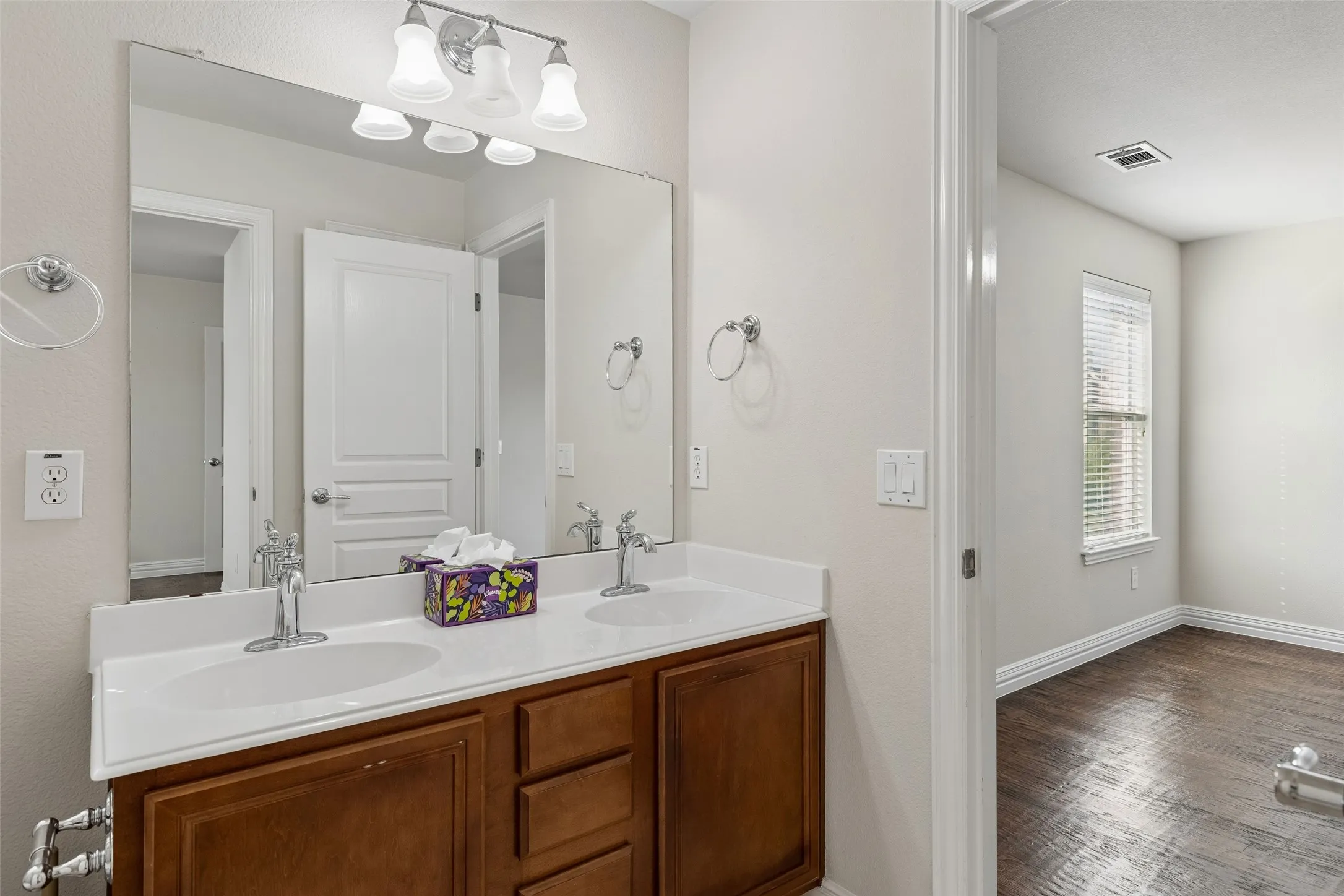 Dual vanity with integrated sinks, wood-finish cabinetry, and a chrome light fixture
