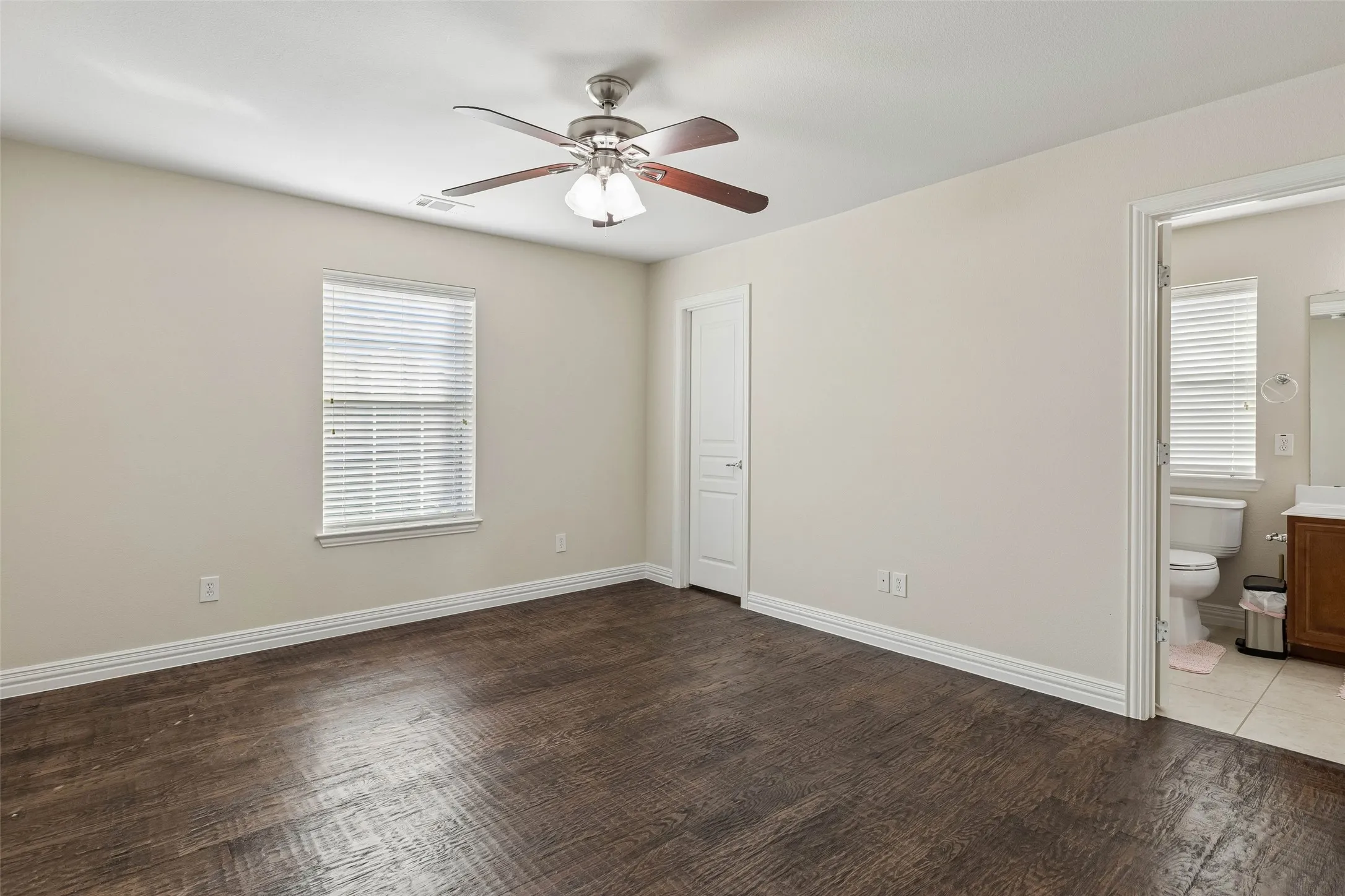 Spacious room featuring wood-finish flooring, a ceiling fan with integrated lighting, and a window with blinds