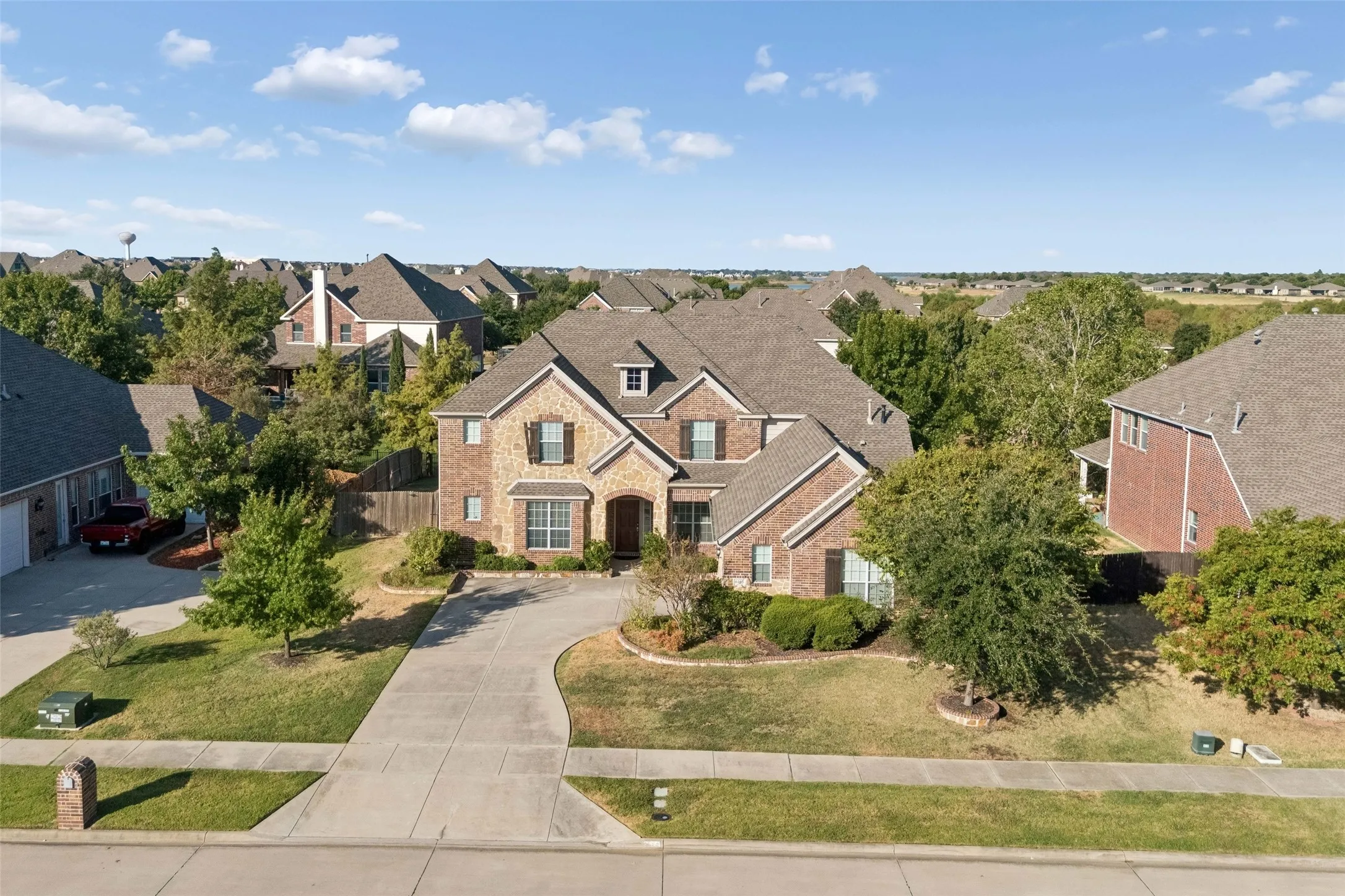 Two-story residence featuring brick and stone exterior, gabled roofline, multiple dormer windows, and a curved driveway