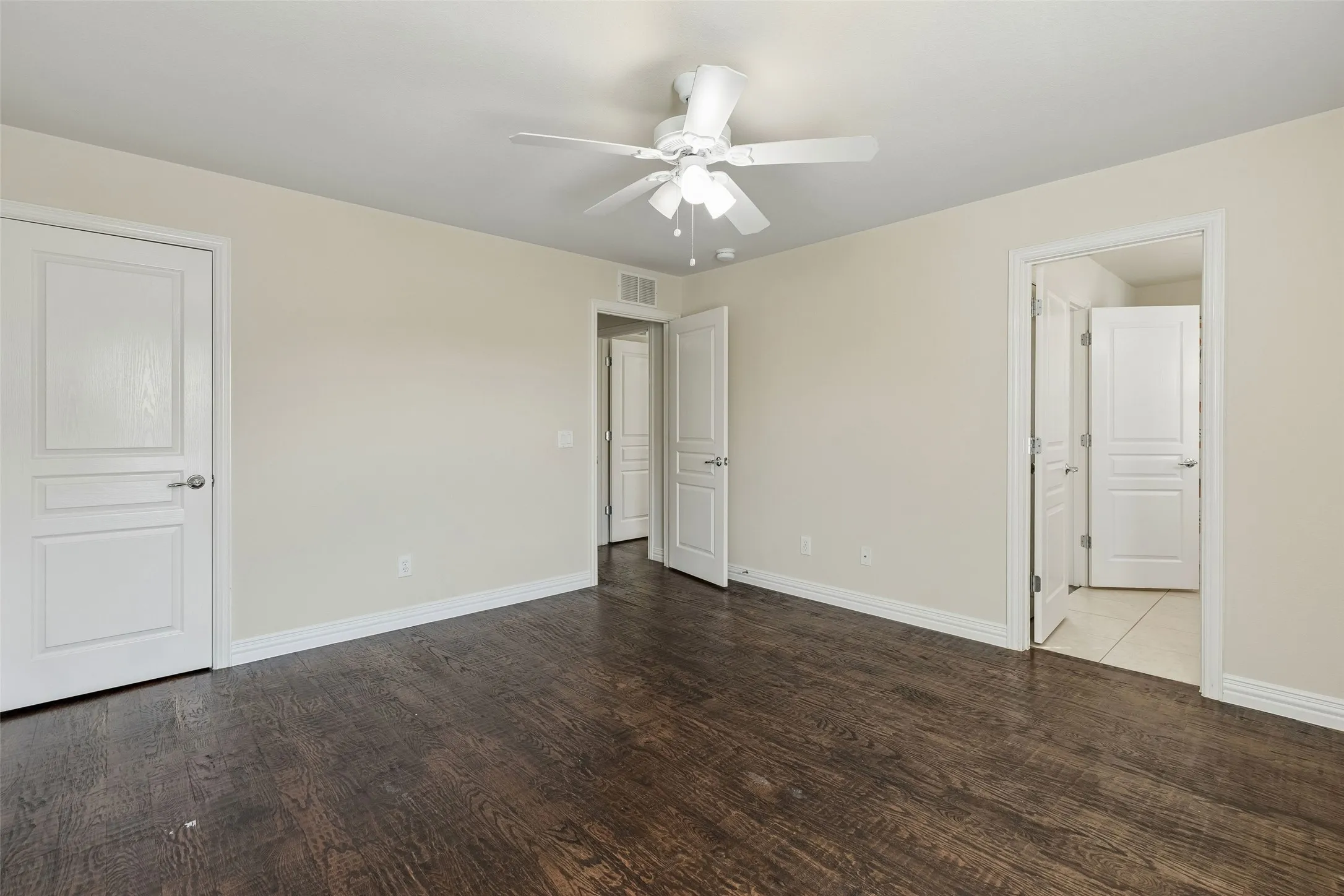 Rich wood-finish flooring, neutral wall tones, white trim, and a ceiling fan with integrated lighting