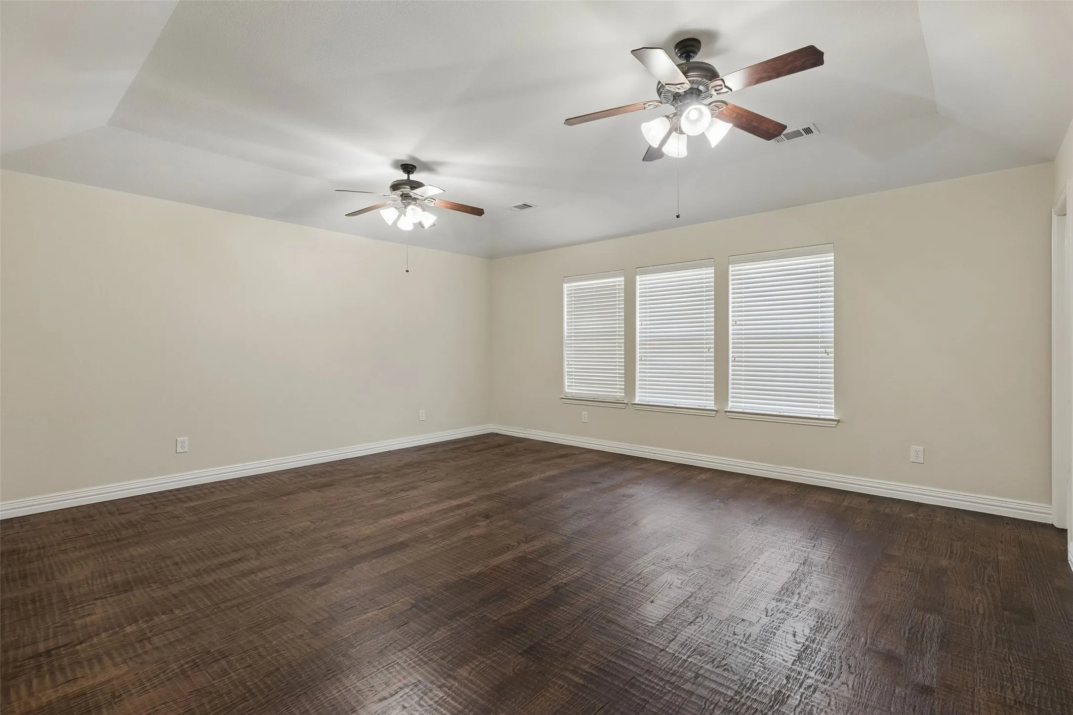 Tray ceiling with two ceiling fans, wood-finish flooring, and multiple windows with blinds