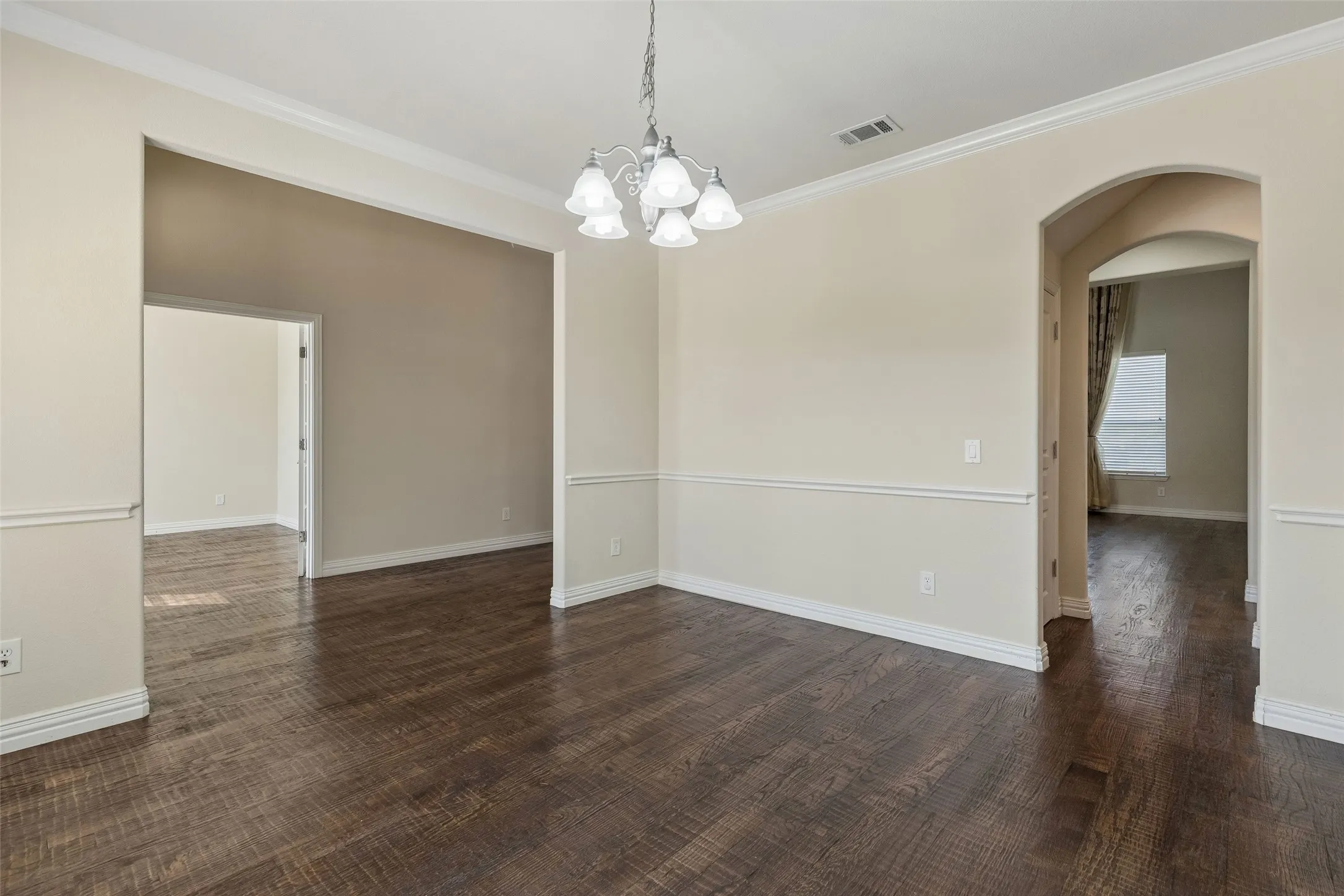 Wood-finish flooring, crown molding, chair rail molding, recessed lighting, and an arched doorway
