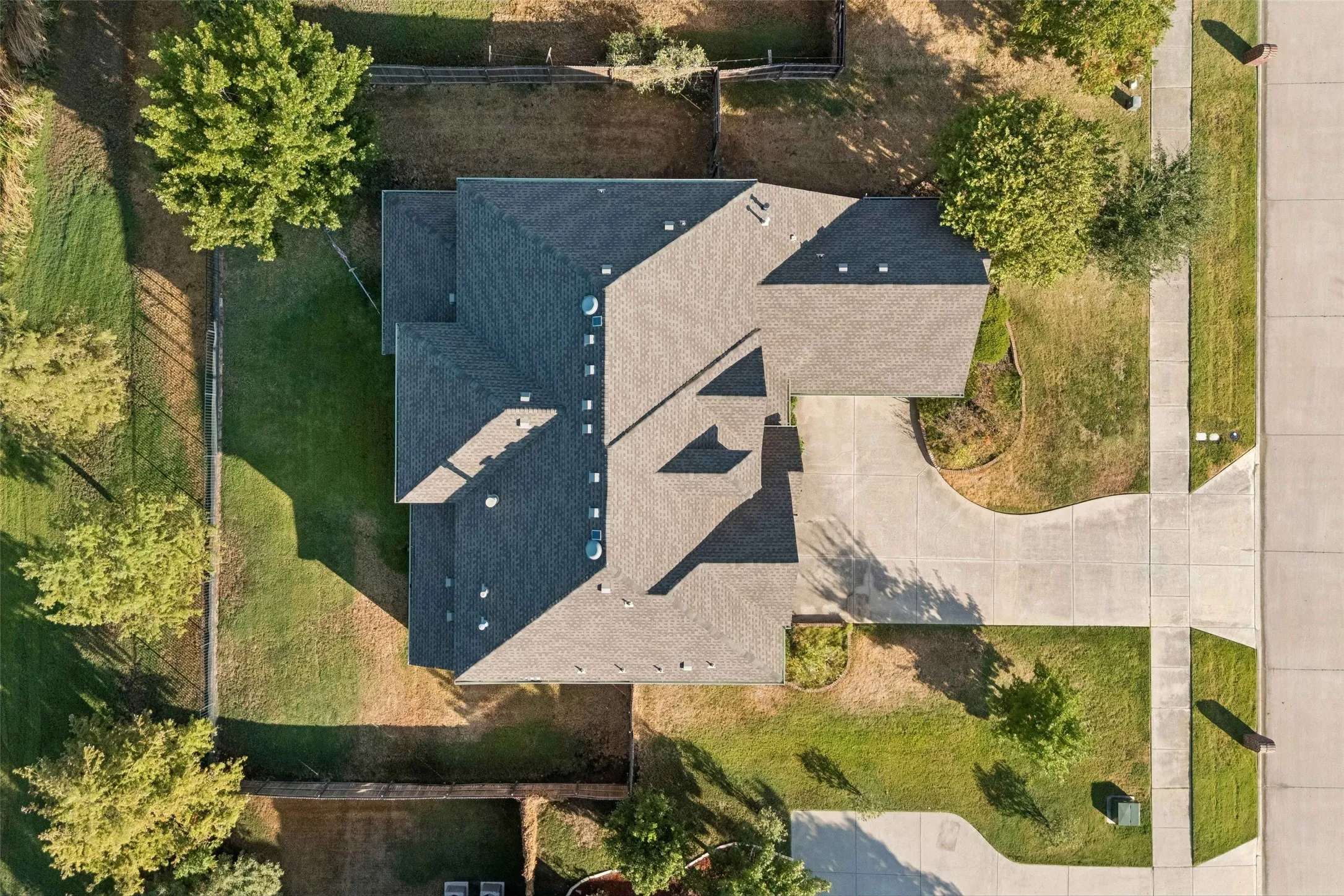Expansive property featuring a shingle roof, mature trees, and a concrete driveway