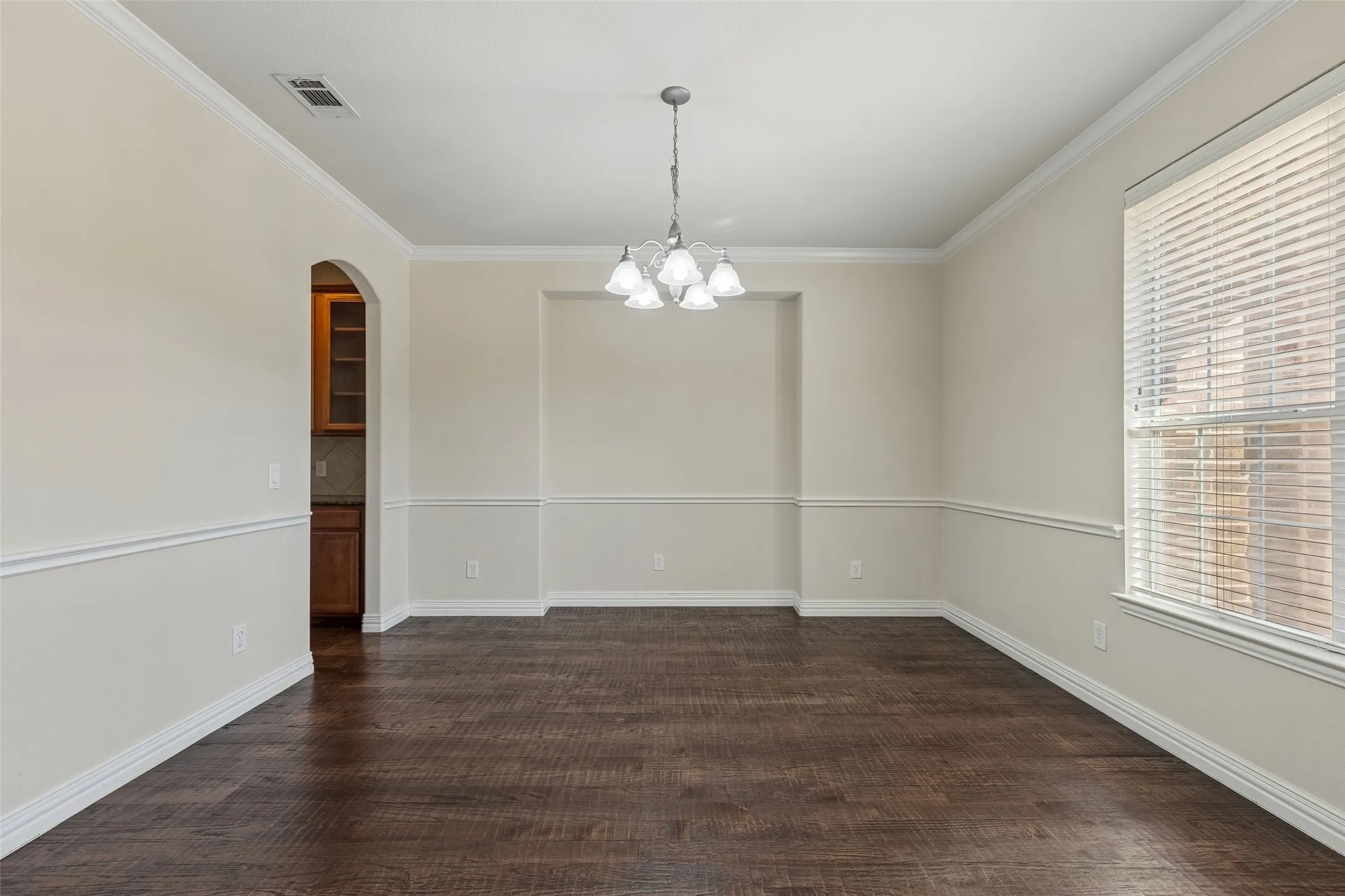 Wood-finish flooring, crown molding, chair rail molding, recessed wall detail, and an arched entryway