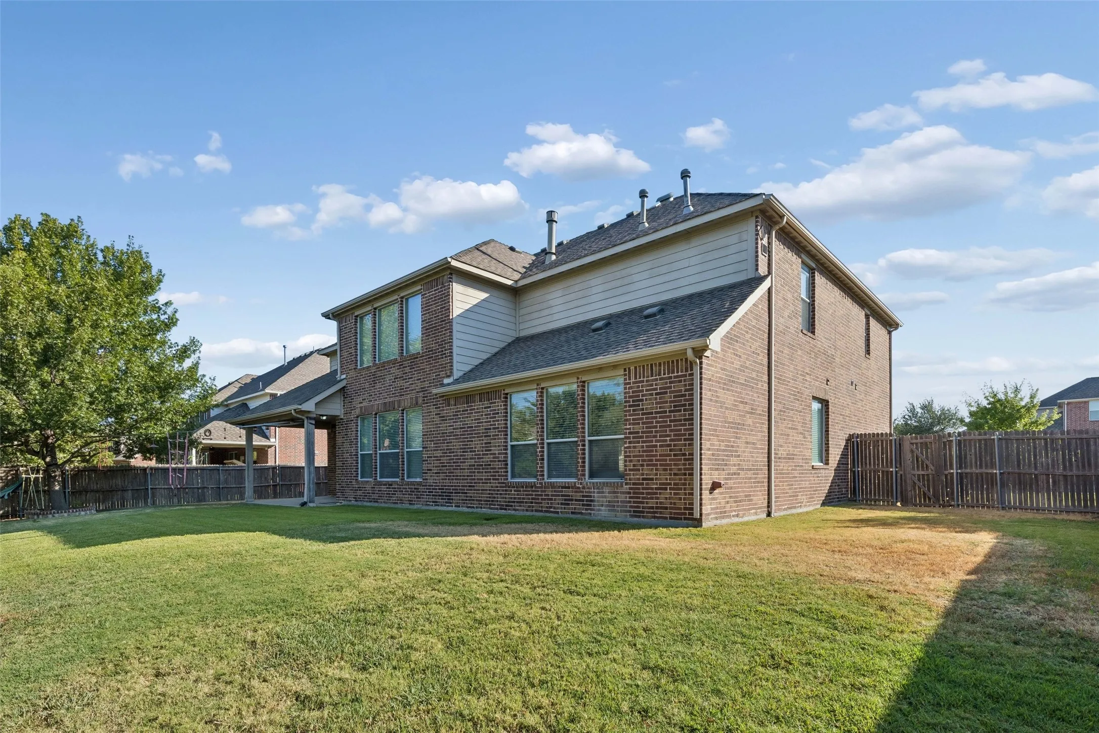 Two-story brick and siding exterior, multiple windows, covered patio, and fenced backyard