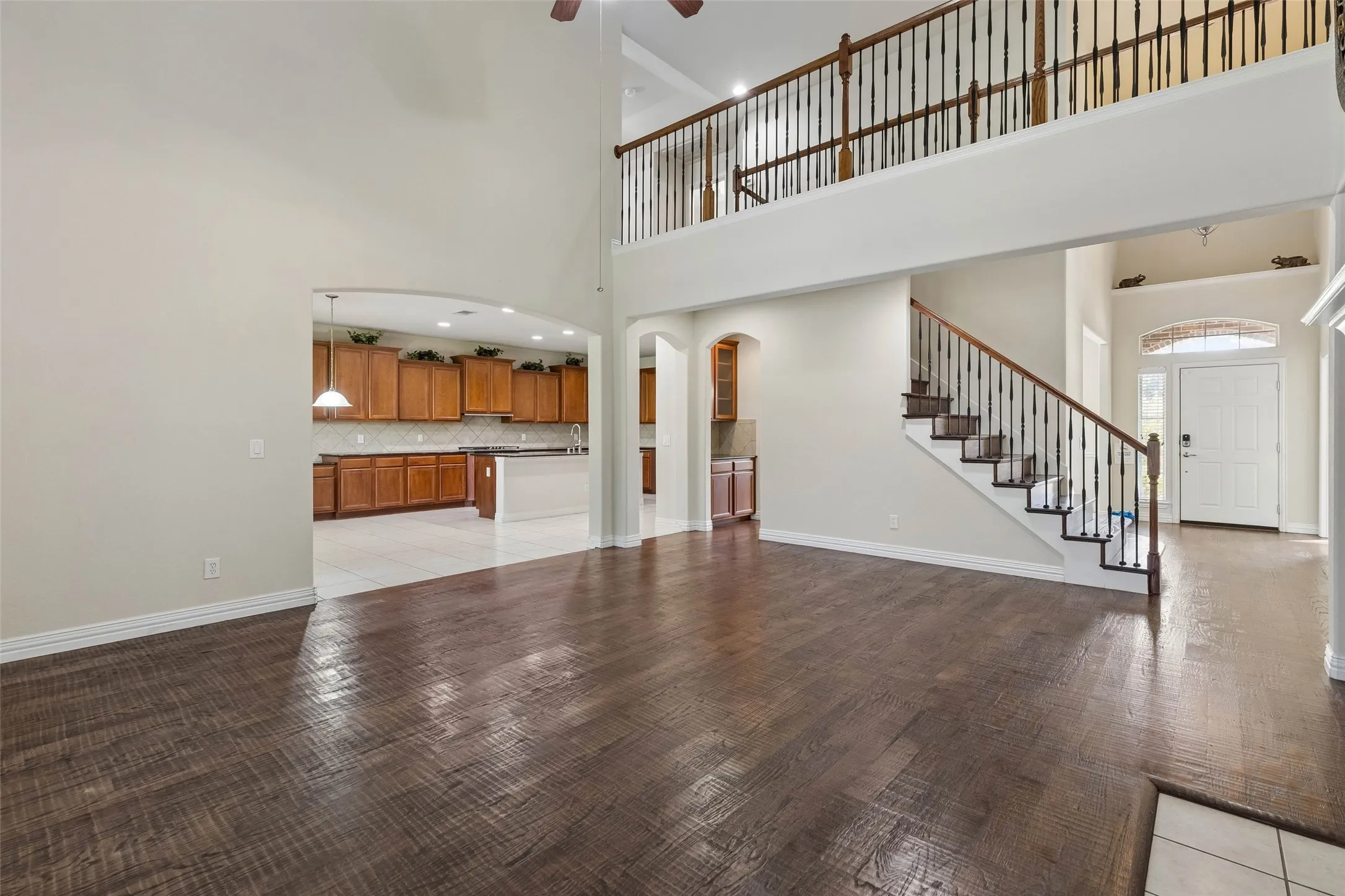 Two-story living space featuring wood-finish flooring, a grand staircase with wrought iron balusters, a second-story landing, and an arched entryway to the kitchen