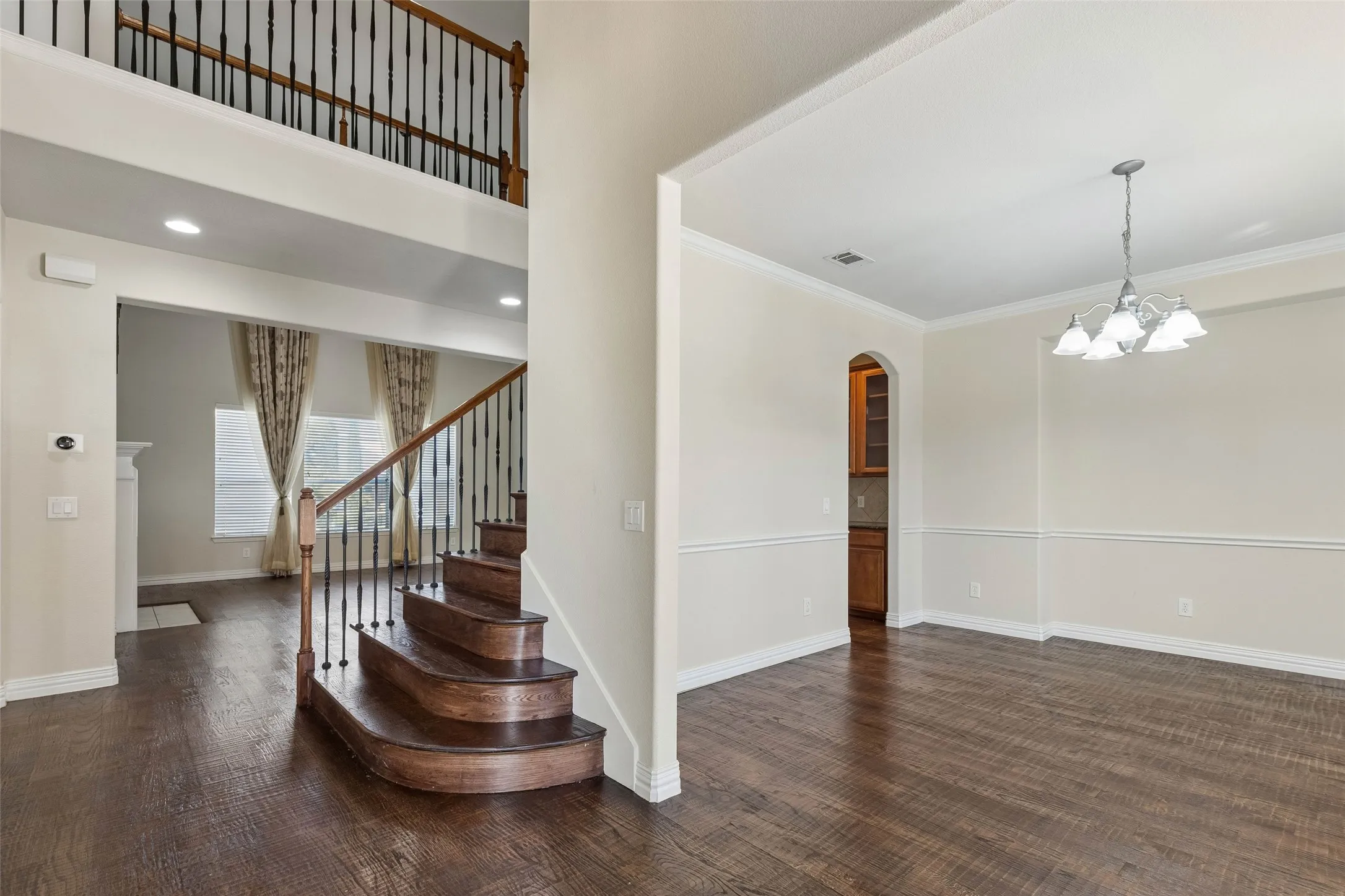 Wood-finish flooring throughout, a curved staircase with wrought iron balusters, crown molding, and an elegant chandelier