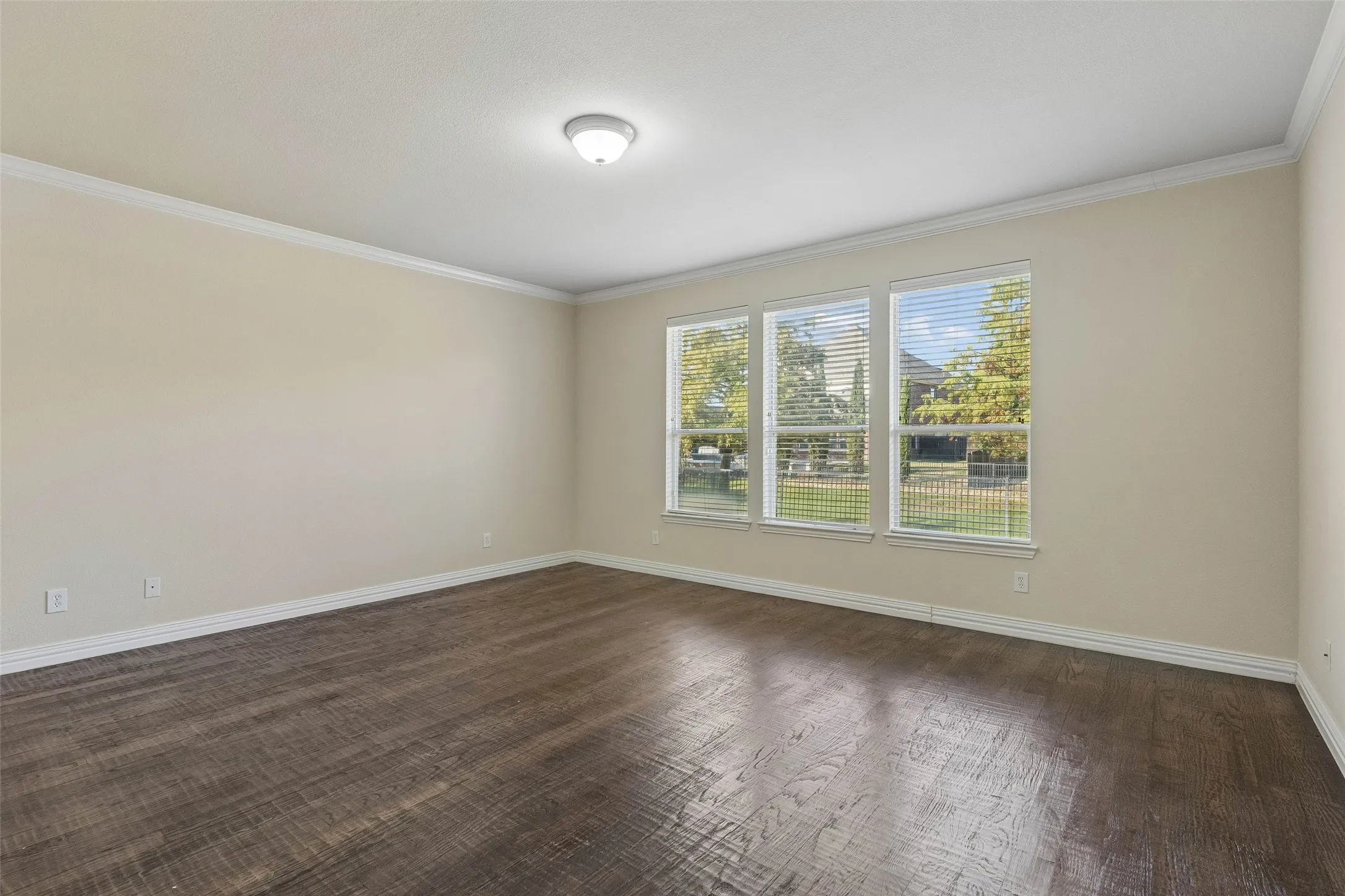 Wood-finish flooring, neutral wall tones, crown molding, and a three-panel window ensemble