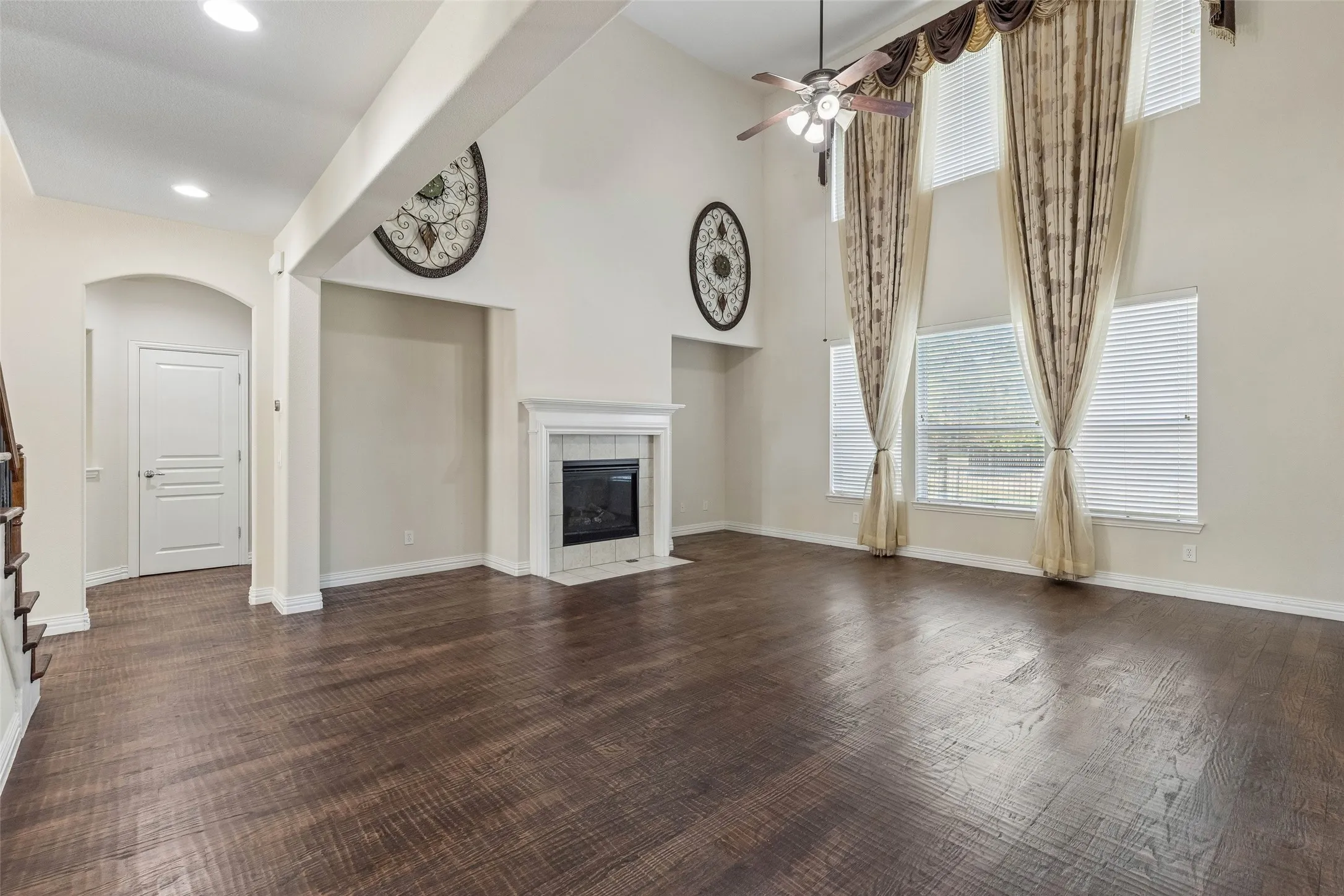 Soaring ceilings with a ceiling fan, a fireplace with a white mantel, large windows, and dark wood-finish flooring