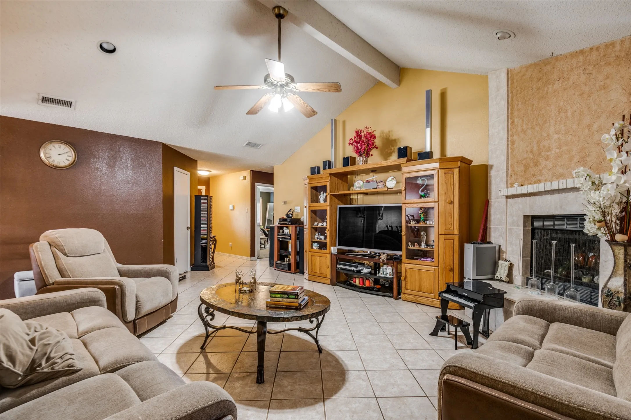 Vaulted ceiling with exposed beam, tile flooring, built-in entertainment center, and a brick-surround fireplace with hearth
