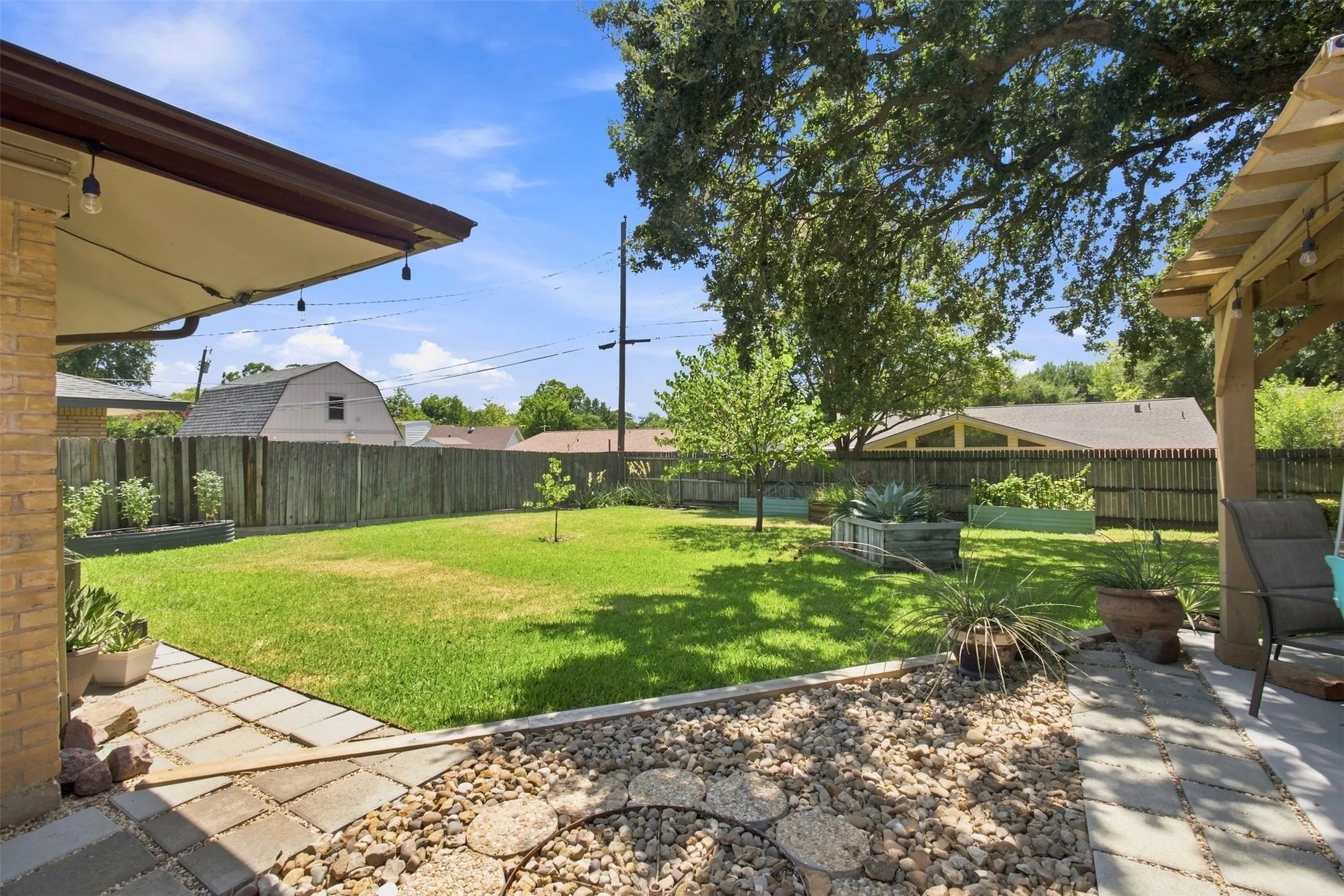Expansive backyard featuring a lush lawn, privacy fencing, multiple raised garden beds, and two distinct patio areas