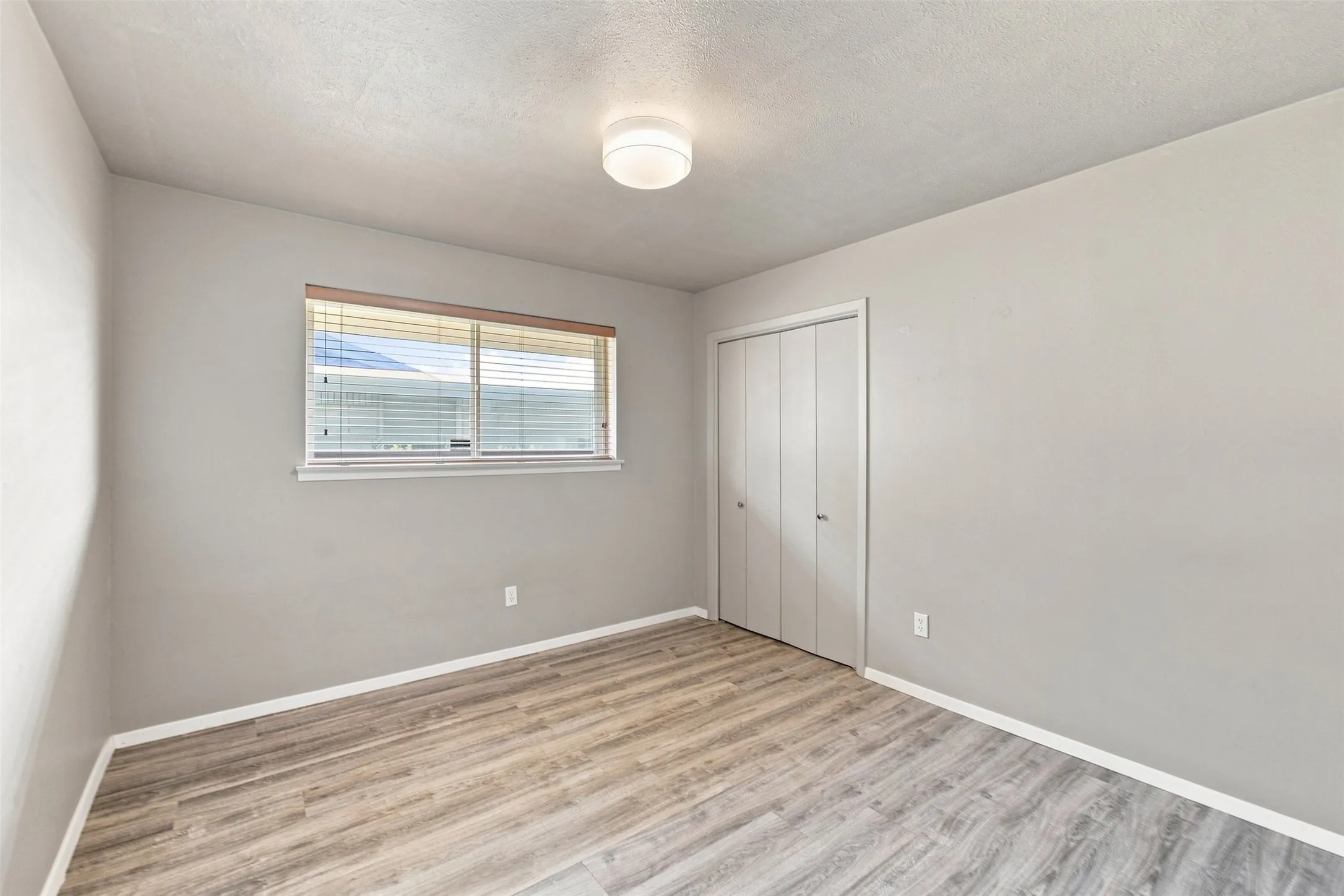 Recessed window with blinds, wood-finish flooring, and bi-fold closet doors